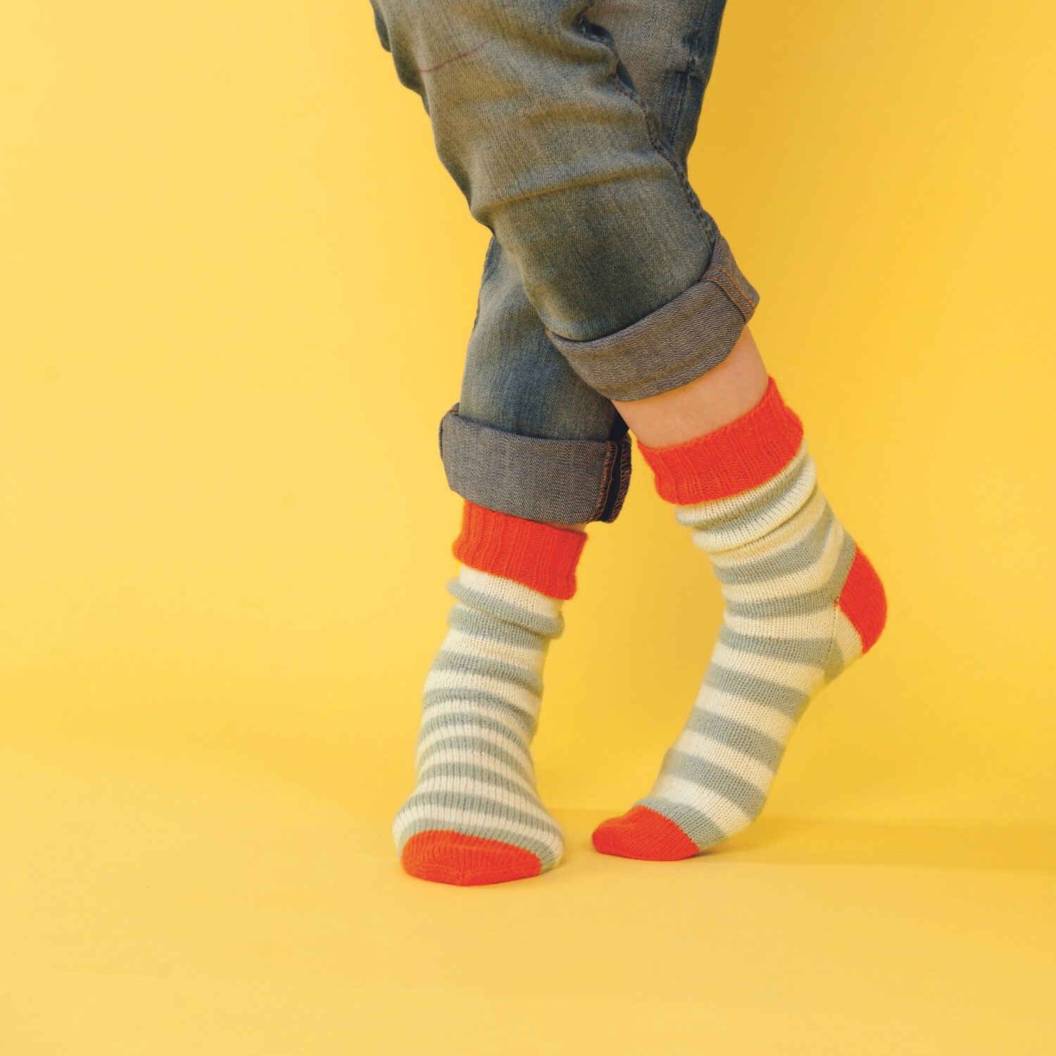 Füße tragen gestrickte Ringelsocken aus weißem, grauem und rotem Garn. 