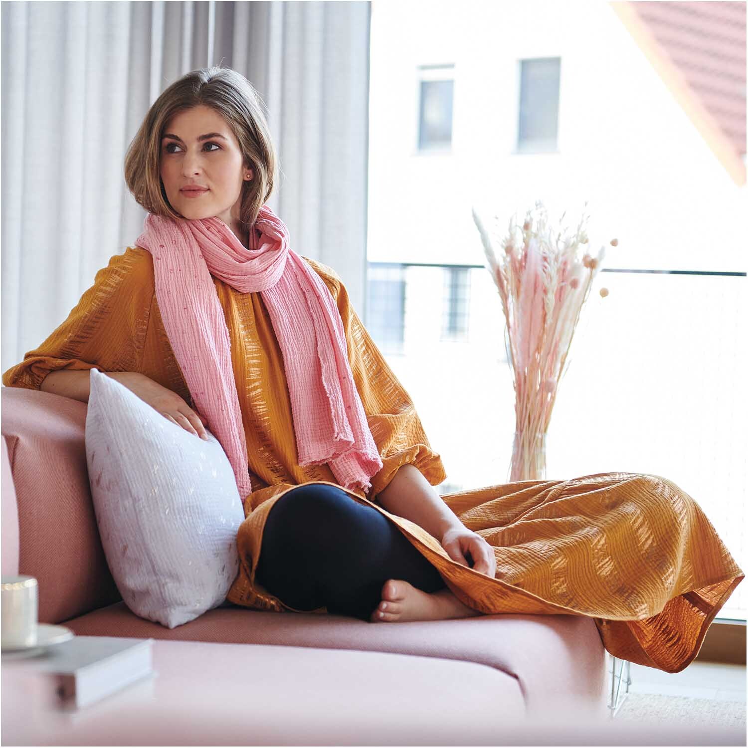 Meterware Krinkelmusselin hellgrau Hot Foil: Frau in gelbem Kleid mit rosa Schal auf rosa Sofa, modernes Wohnzimmer.