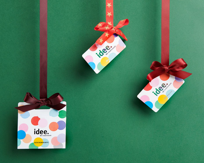 Drei Geschenkkarten hängen an unterschiedlichen roten Bändern mit Schleife vor einem dunkelgrünen Hintergrund.
