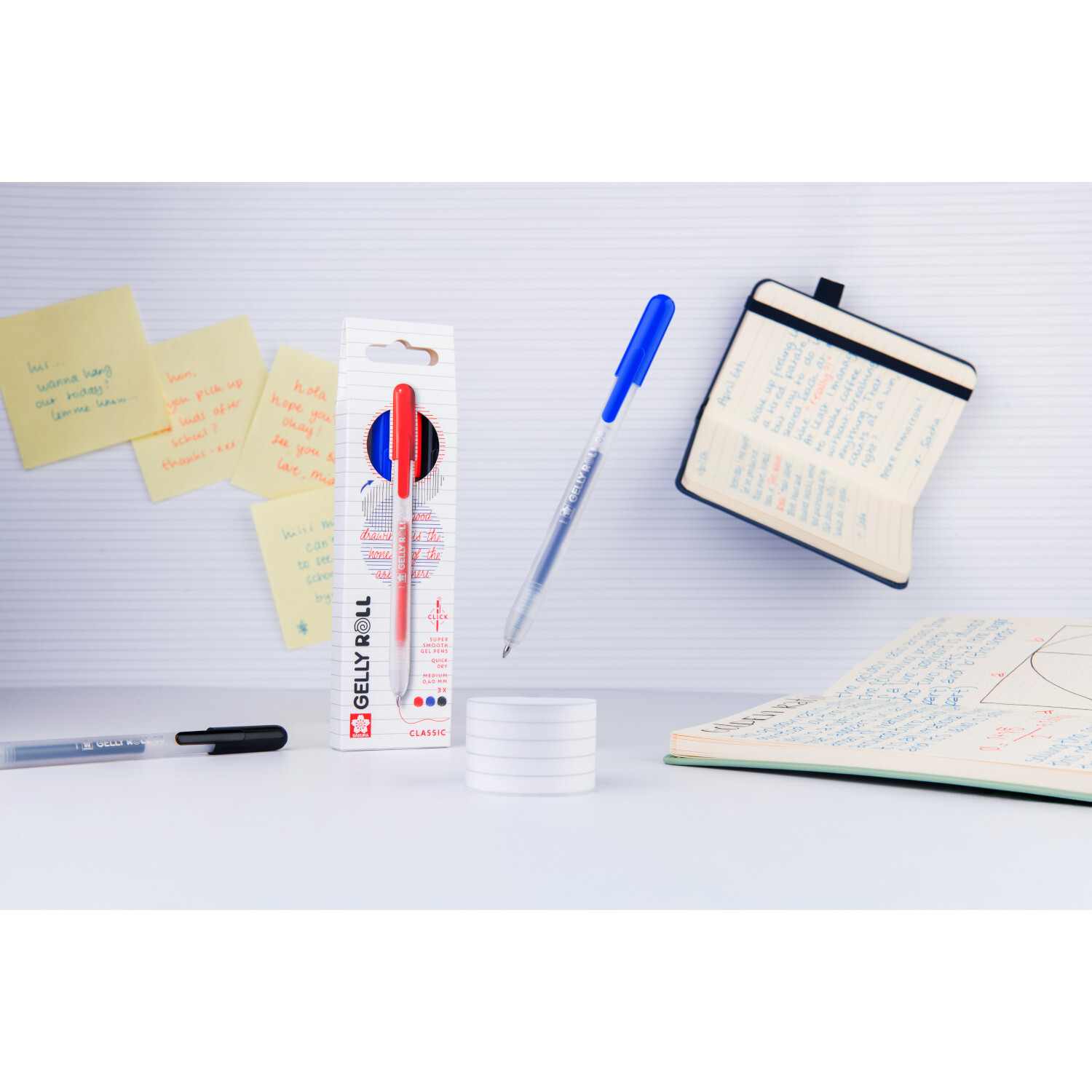 Gelly Roll Retractable Set Classic von SAKURA: Drei Stifte in verschiedenen Farben, umgeben von Notizbüchern und Haftnotizen.