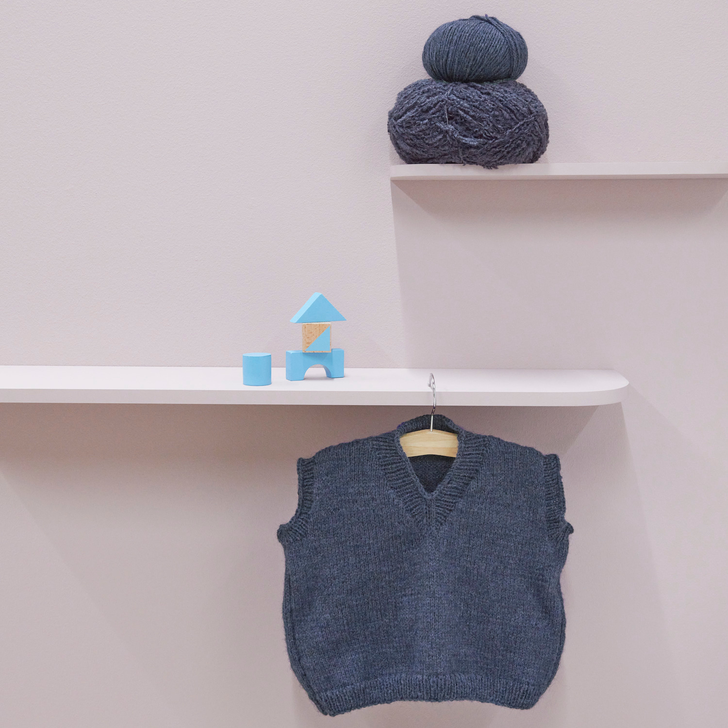 Rico Kids 13: Kinderpullunder in Marineblau aus weicher Alpaka-Wolle, präsentiert auf einem Regal mit passendem Garn und Spielzeug.