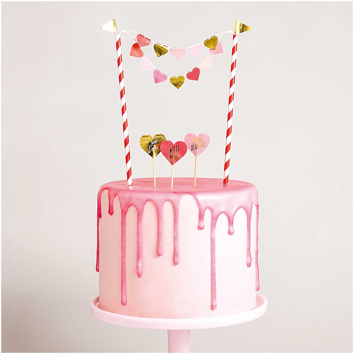 Kuchendekoration Herzen von Rico Design: Rosa Torte mit Herz-Dekorationen und Streifenstangen.