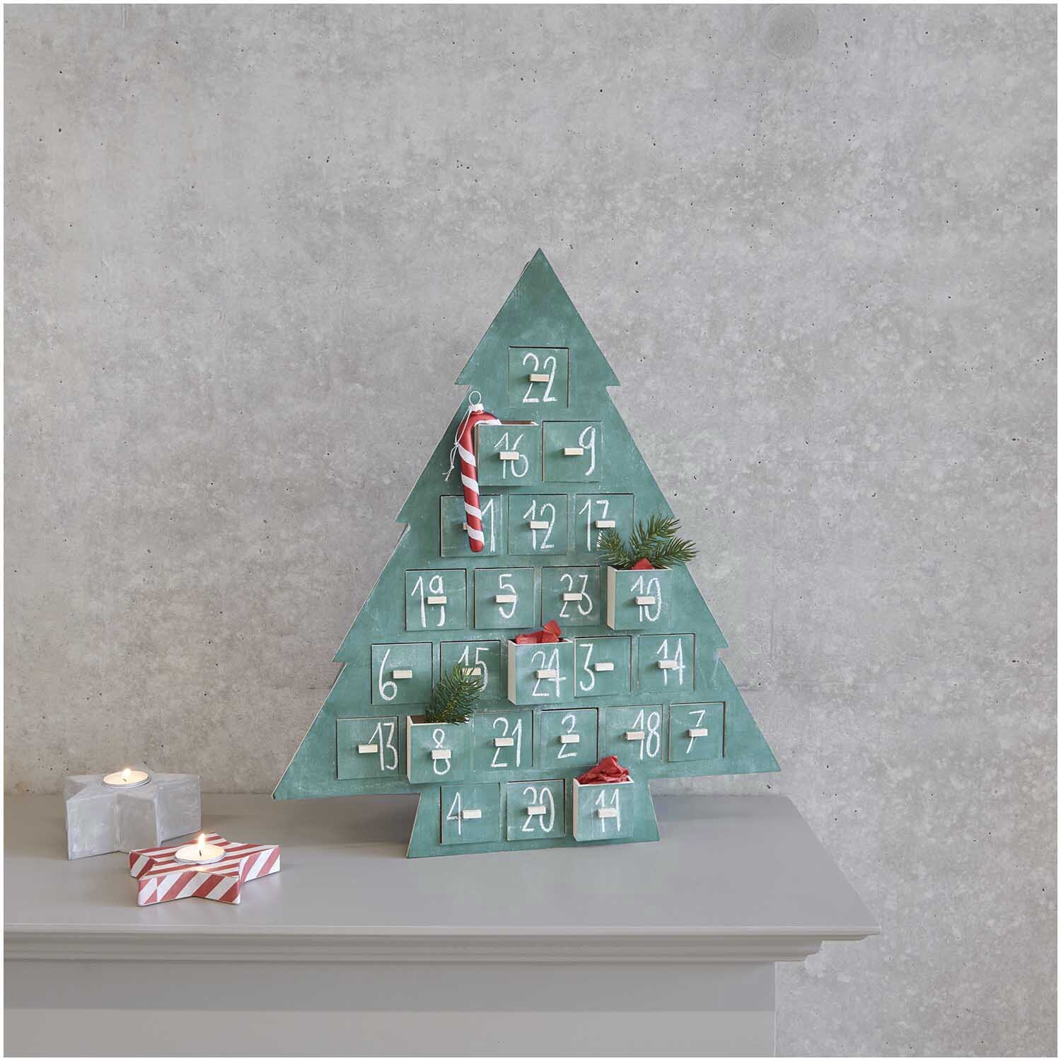 Adventskalender Tanne aus Holz mit 24 nummerierten Fächern, dekoriert mit Zweigen und Zuckerstangen, von Rico Design.