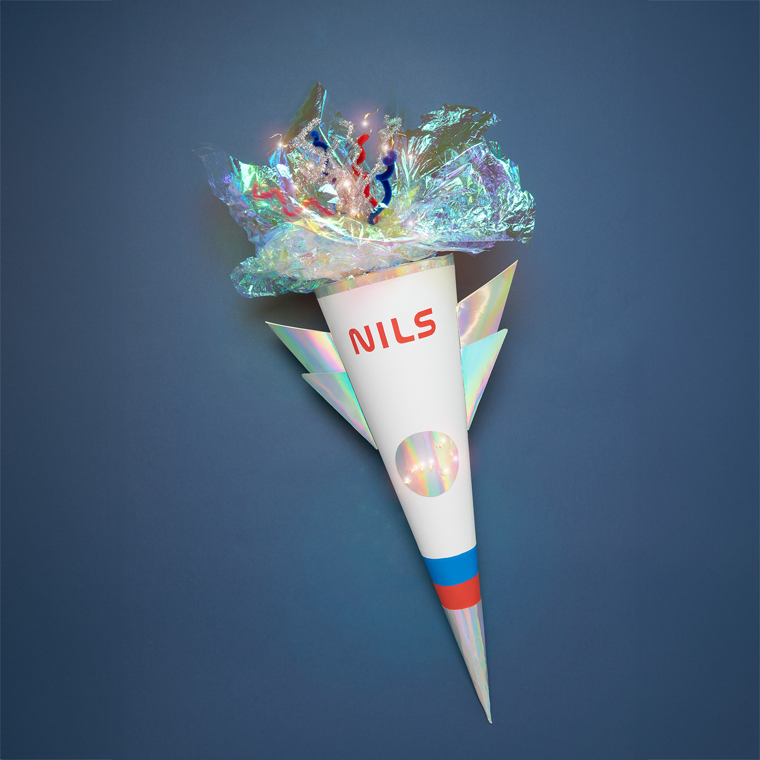 Bastelanleitung Schultüte Rakete: Weiße Schultüte in Raketenform mit buntem Dekor auf blauem Hintergrund.