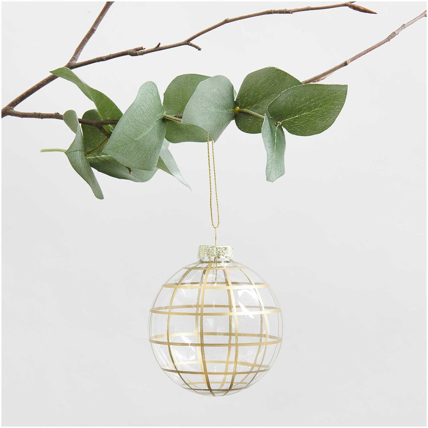 Glaskugel Baumschmuck grafisch gold Ø 8cm von Rico Design, hängend an einem Ast mit grünen Blättern.