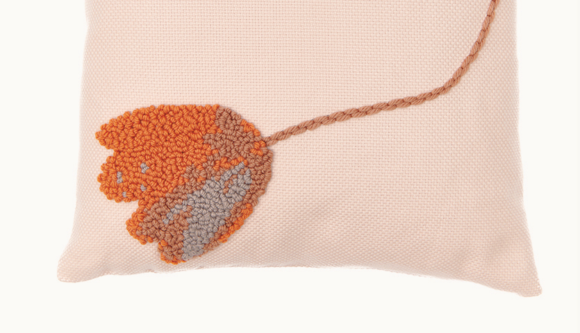 Punch Needle Anleitung Kissen mit Blumenmotiv zeigt ein Kissen mit orange-grauem Blumenmuster auf beigem Hintergrund.