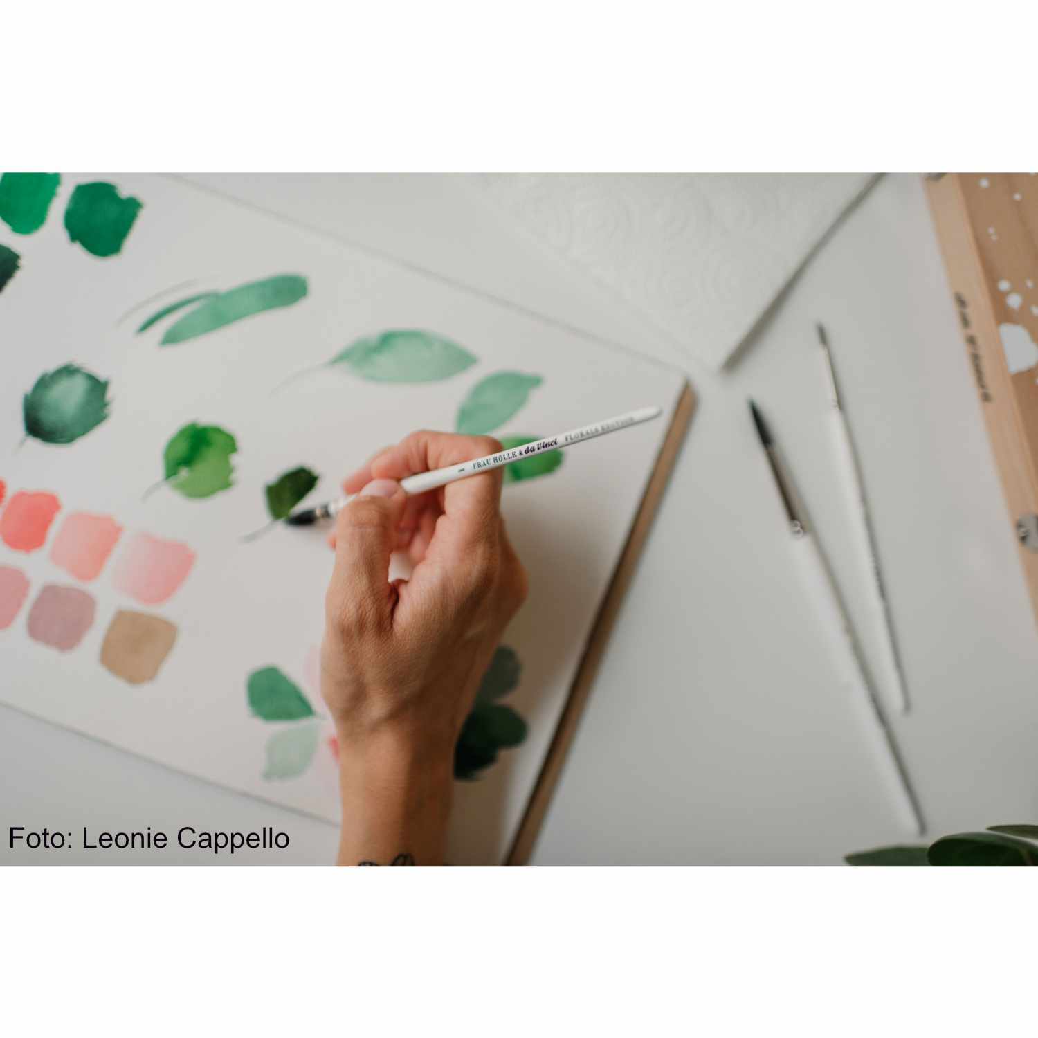 da Vinci Pinsel-Set Loose Watercolor Florals: Hand hält Pinsel über Palette mit grünen und rosa Farbtönen. Ideal für Aquarellmalerei.