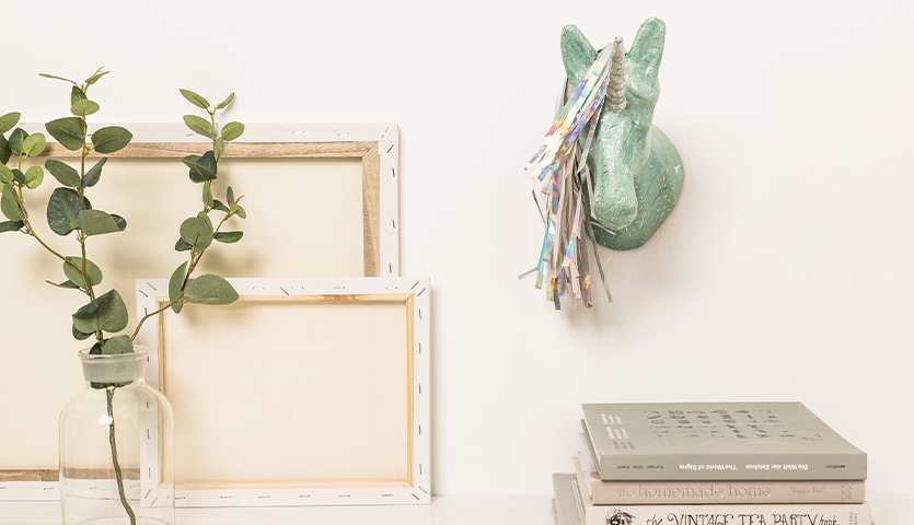 Bastelanleitung Pappmache-Einhorn: Ein grüner Einhornkopf aus Pappmaché an einer weißen Wand, dekoriert mit buntem Papier.