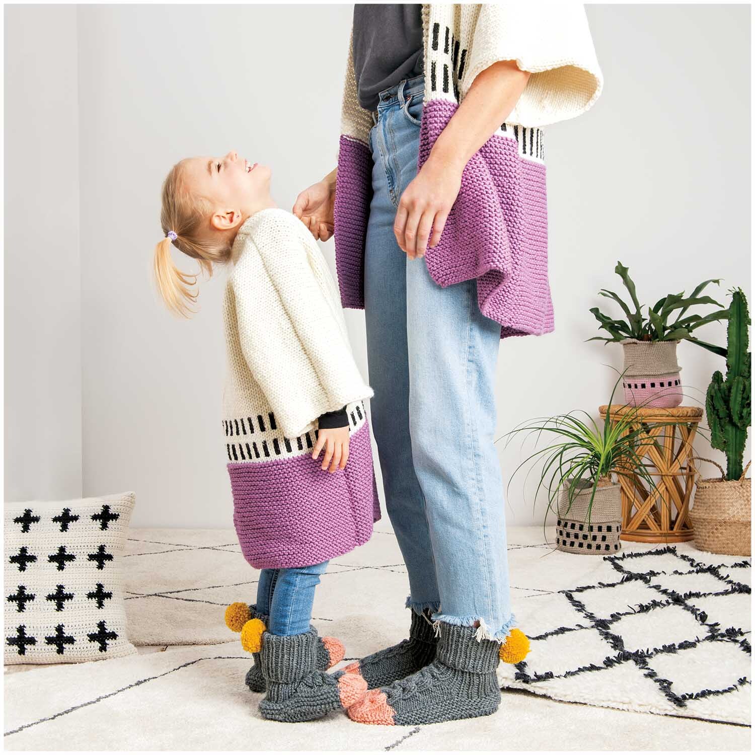Essentials Mega Wool chunky: Mutter und Kind in gestrickten Cardigans, lila und creme, auf gemustertem Teppich.