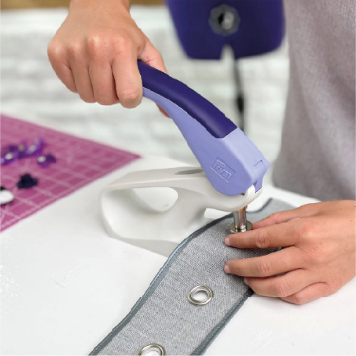 Vario Creative Tool - Stanzwerkzeug von Prym in Blau beim Stanzen von Ösen in grauen Stoff.