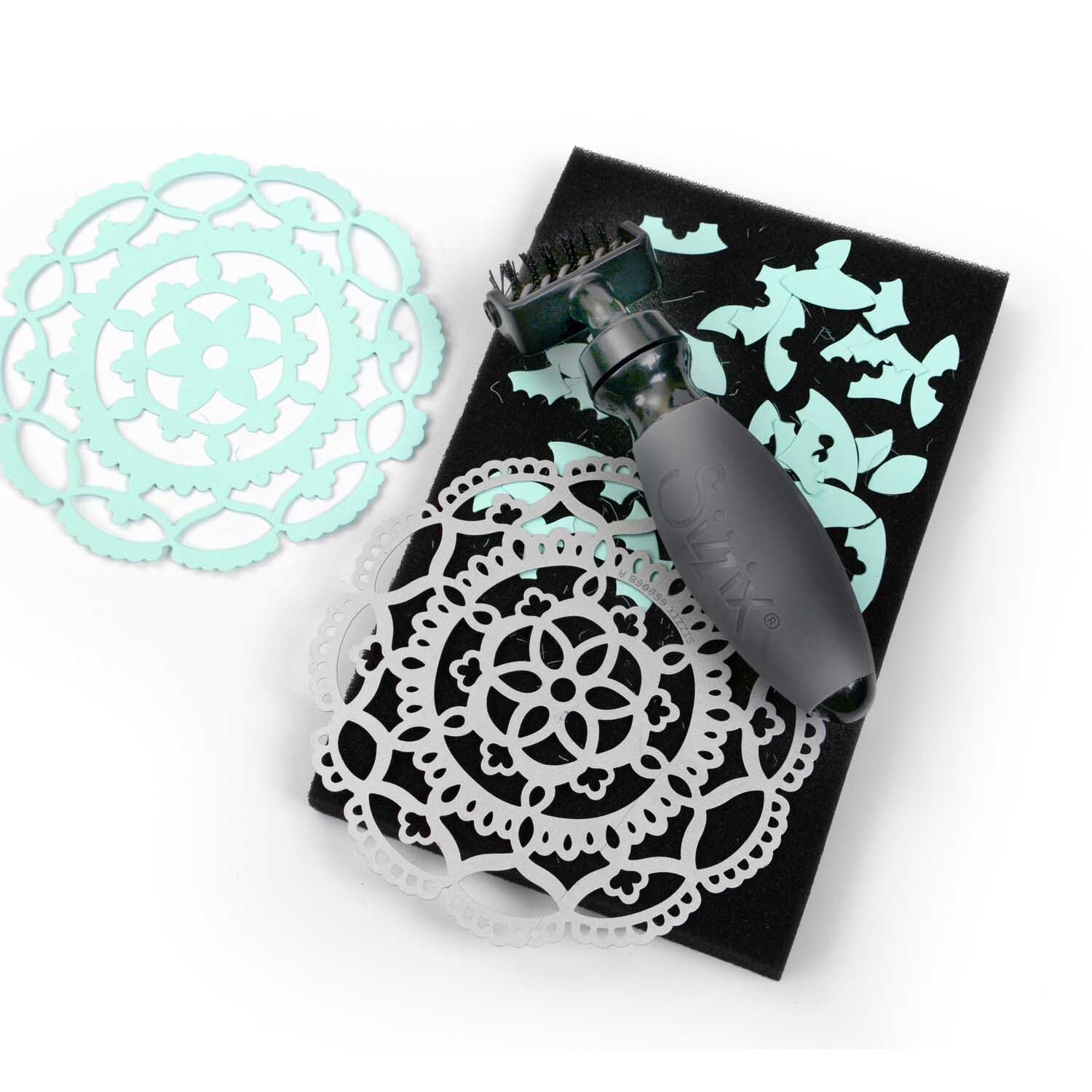 Brush & Foam Pad von Sizzix: Ein schwarzes Werkzeug mit Schaumstoffunterlage und filigranen, blauen Papiermustern.