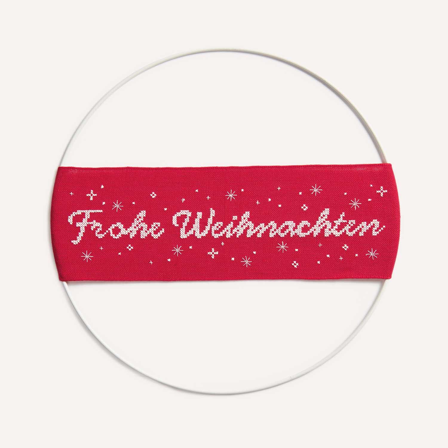 Stickanleitung Frohe Weihnachten Wanddeko: Rotes Banner mit weißem Schriftzug und Schneeflocken.