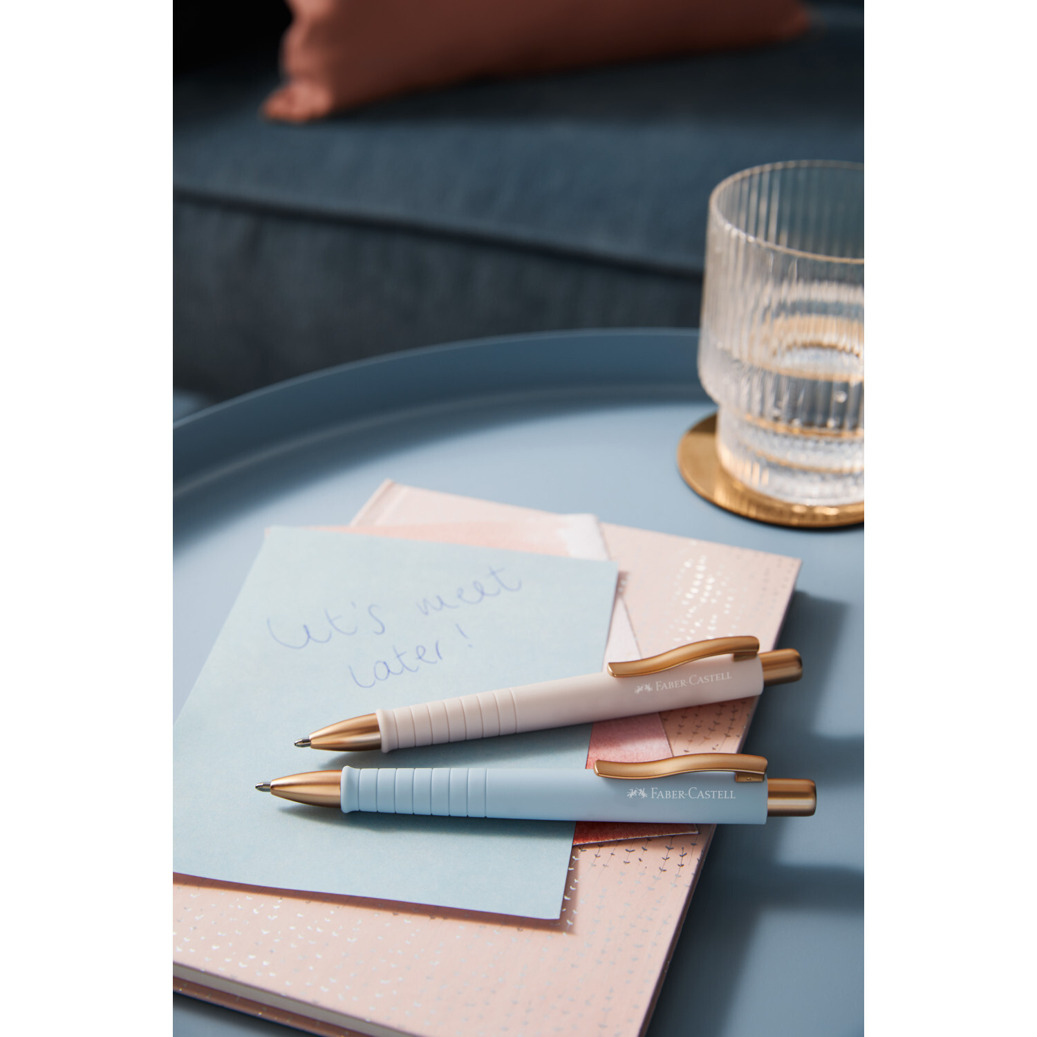 Kugelschreiber Poly Ball Urban XB auf blauem Tisch mit Notizbuch und Glas, Faber Castell.