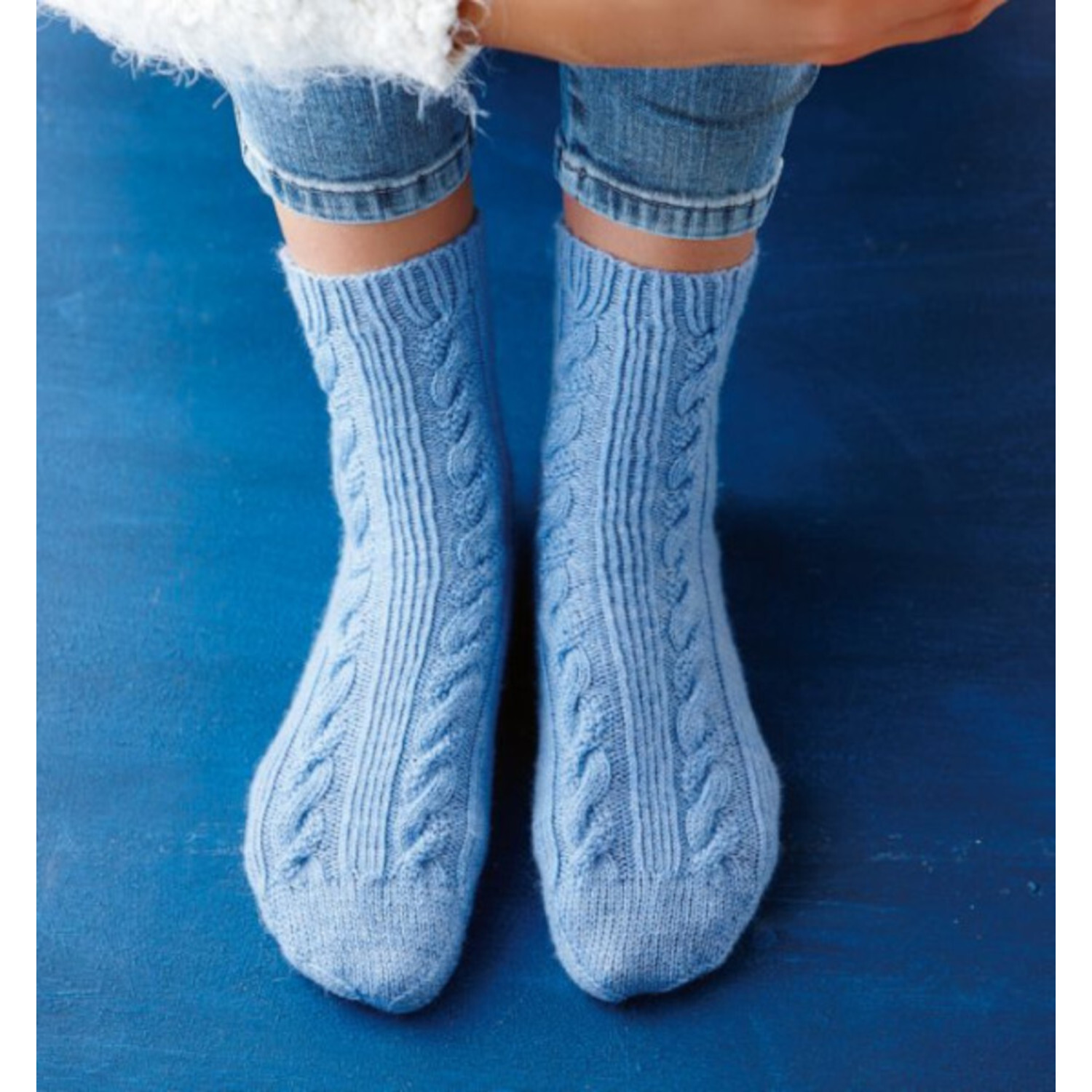 Das ultimative Socken-Strickbuch: Hellblaue, handgestrickte Socken mit Zopfmuster auf blauem Hintergrund.