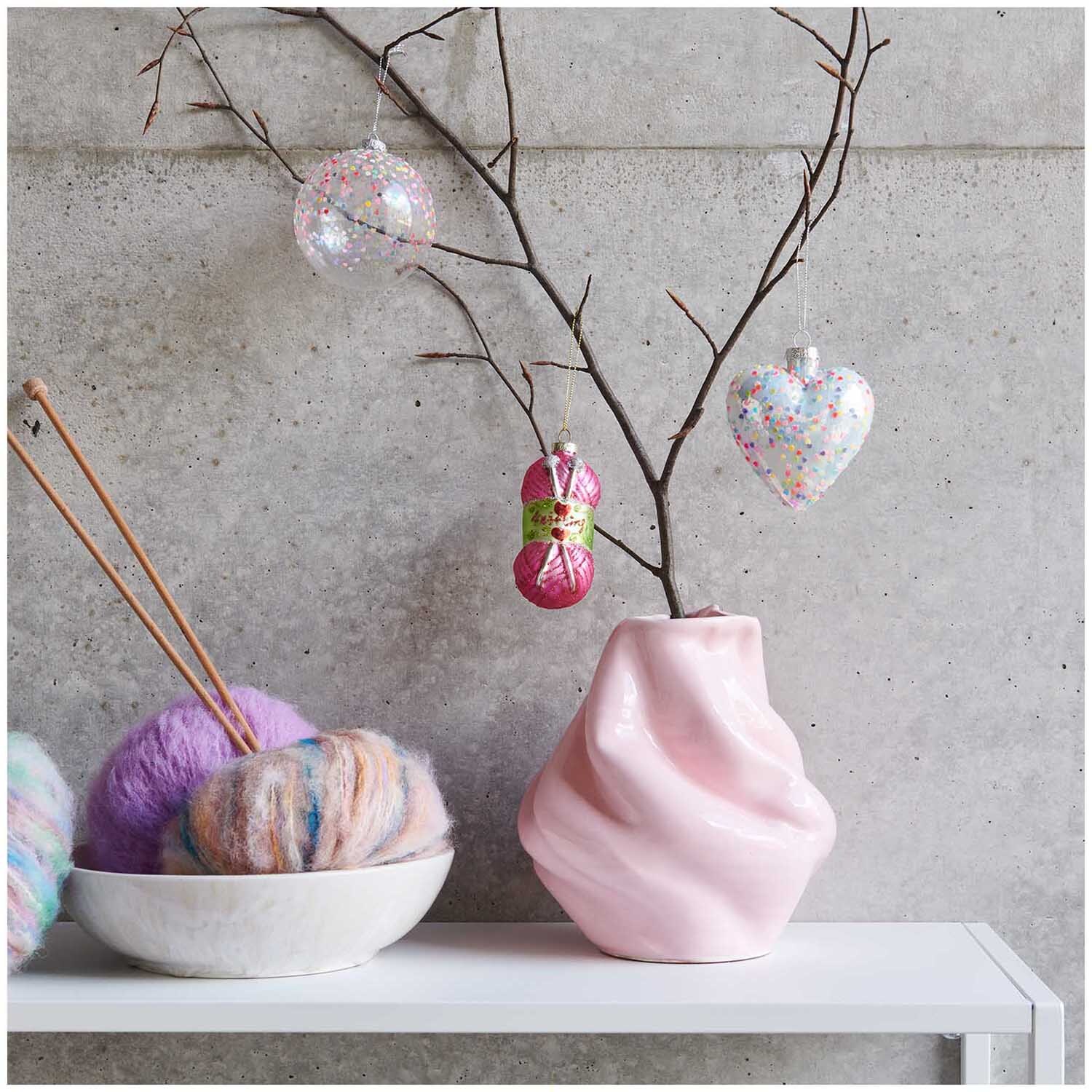 Glaskugel Baumschmuck Wollknäuel an einem Ast in rosa Vase, dekoriert mit bunten Garnen.