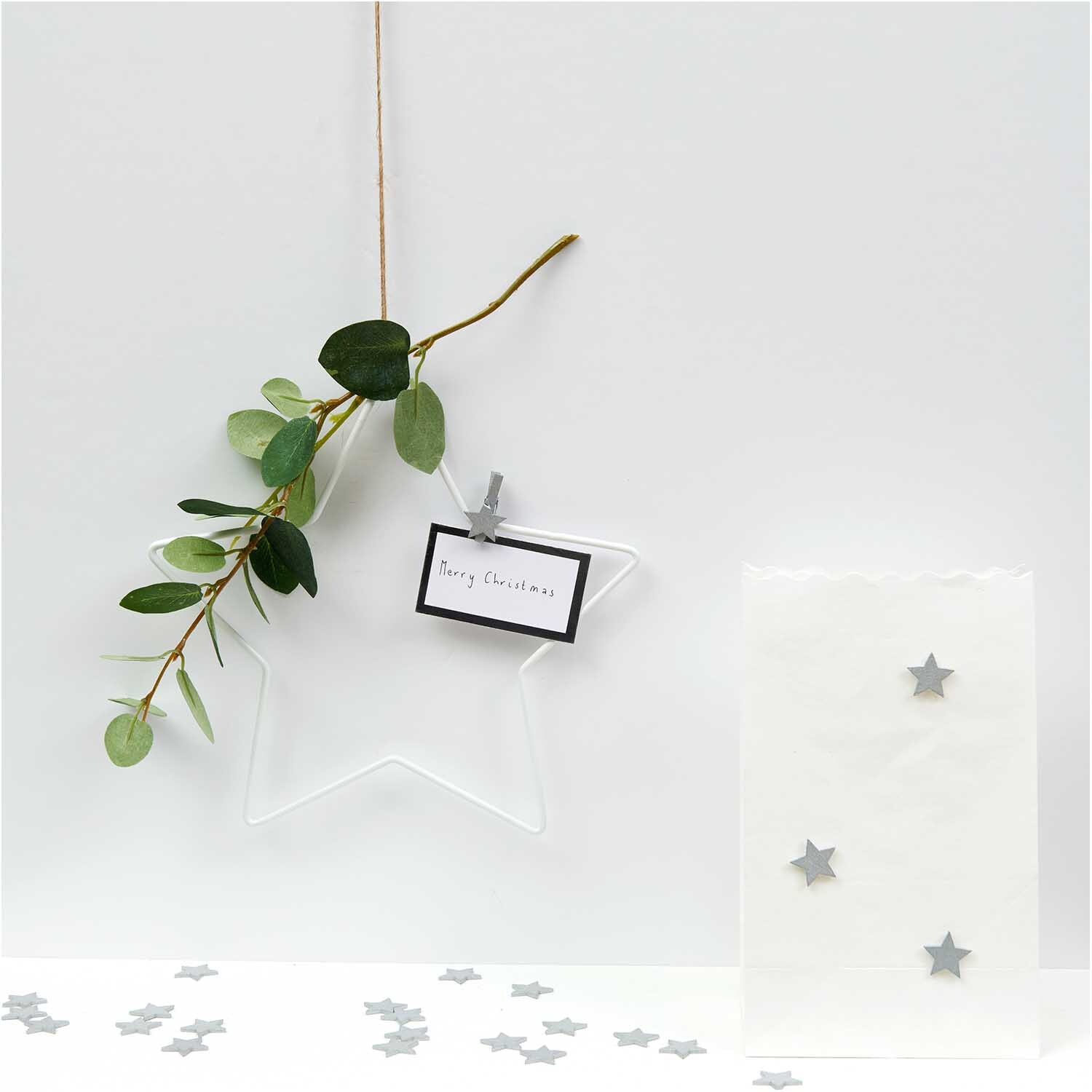 Holzsticker Sterne silber 20x19mm 24 Stück von Rico Design, dekorativ arrangiert mit Zweig und Geschenktüte.