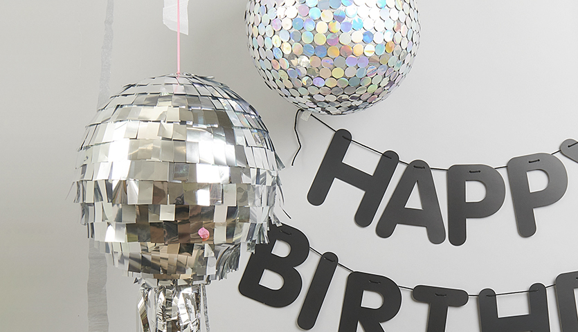 Bastelanleitung Diskokugel: Zwei glänzende Diskokugeln und ein "Happy Birthday"-Banner an der Wand.