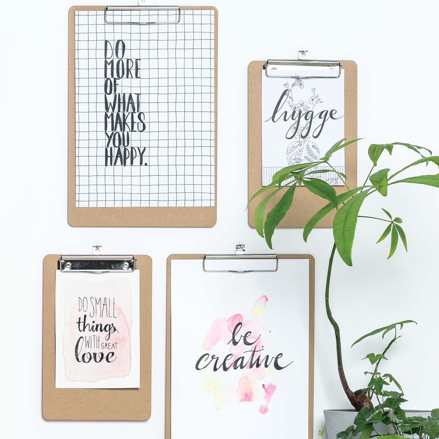 Anleitung Wanddeko Handlettering-Kunstwerke: Vier Klemmbretter mit inspirierenden Sprüchen, dekoriert mit einer Pflanze im Hintergrund.