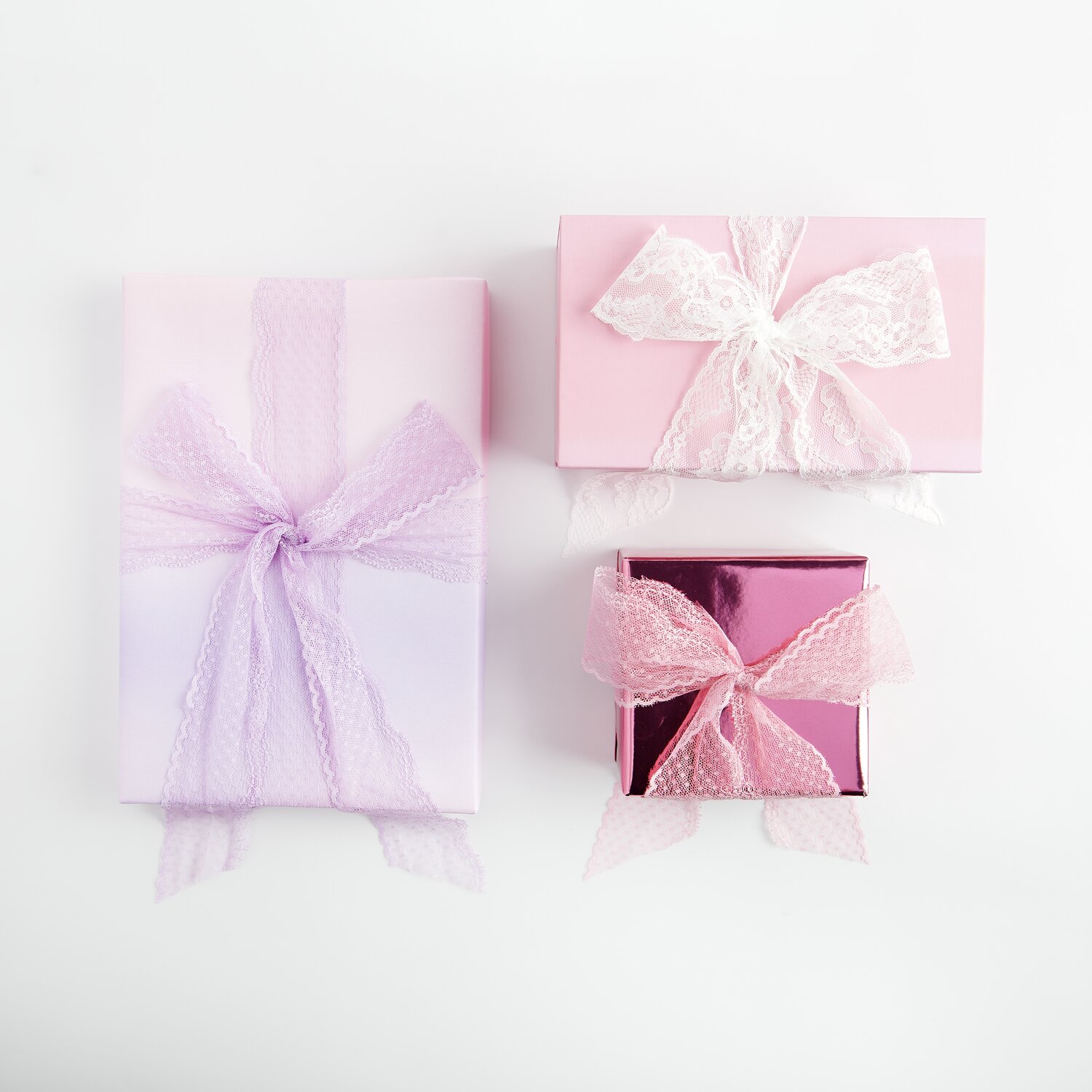 Paper Poetry Spitzenband Pünktchen: Drei Geschenke mit Spitzenband in Rosa, Flieder und Off-White verziert.