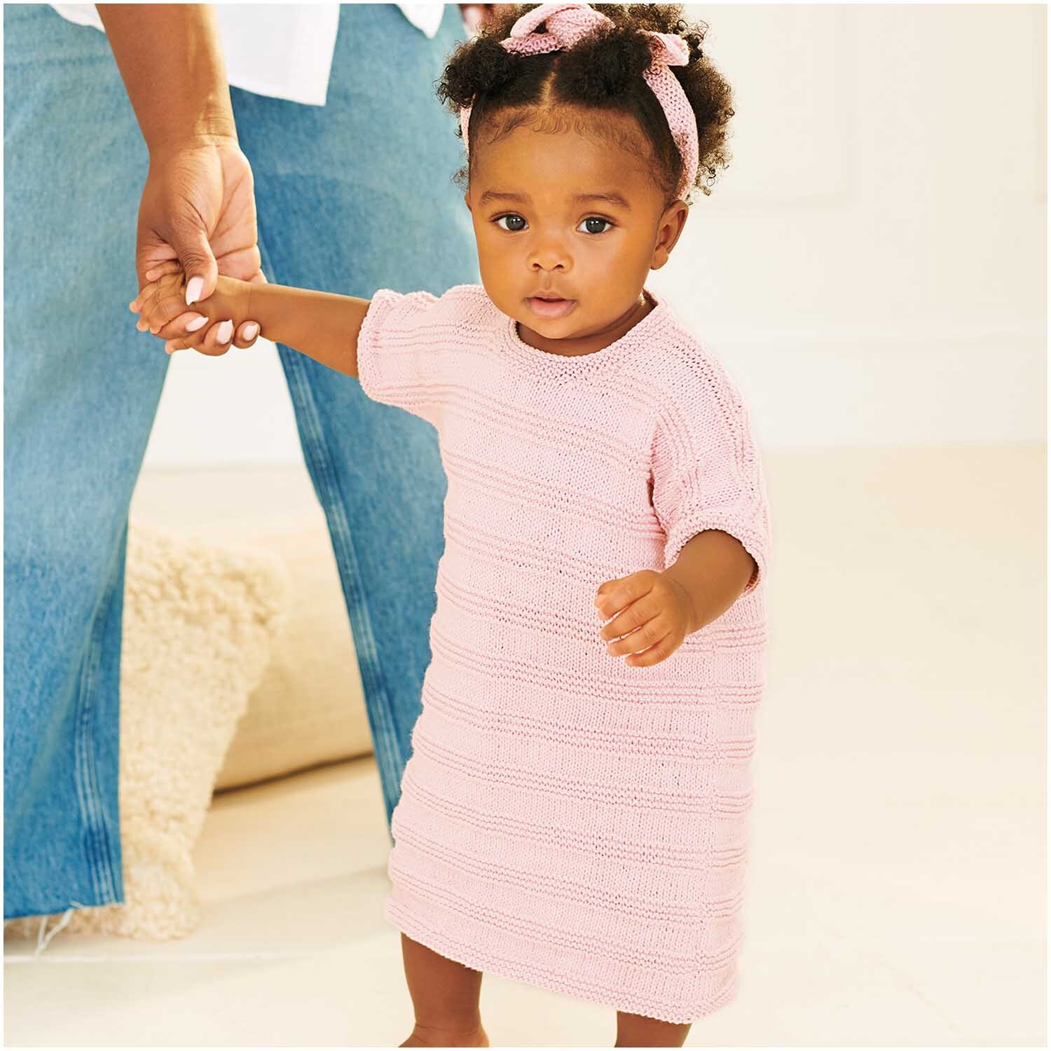Baby Organic Cotton: Ein Kleinkind trägt ein rosa Strickkleid, gehalten von einem Erwachsenen.