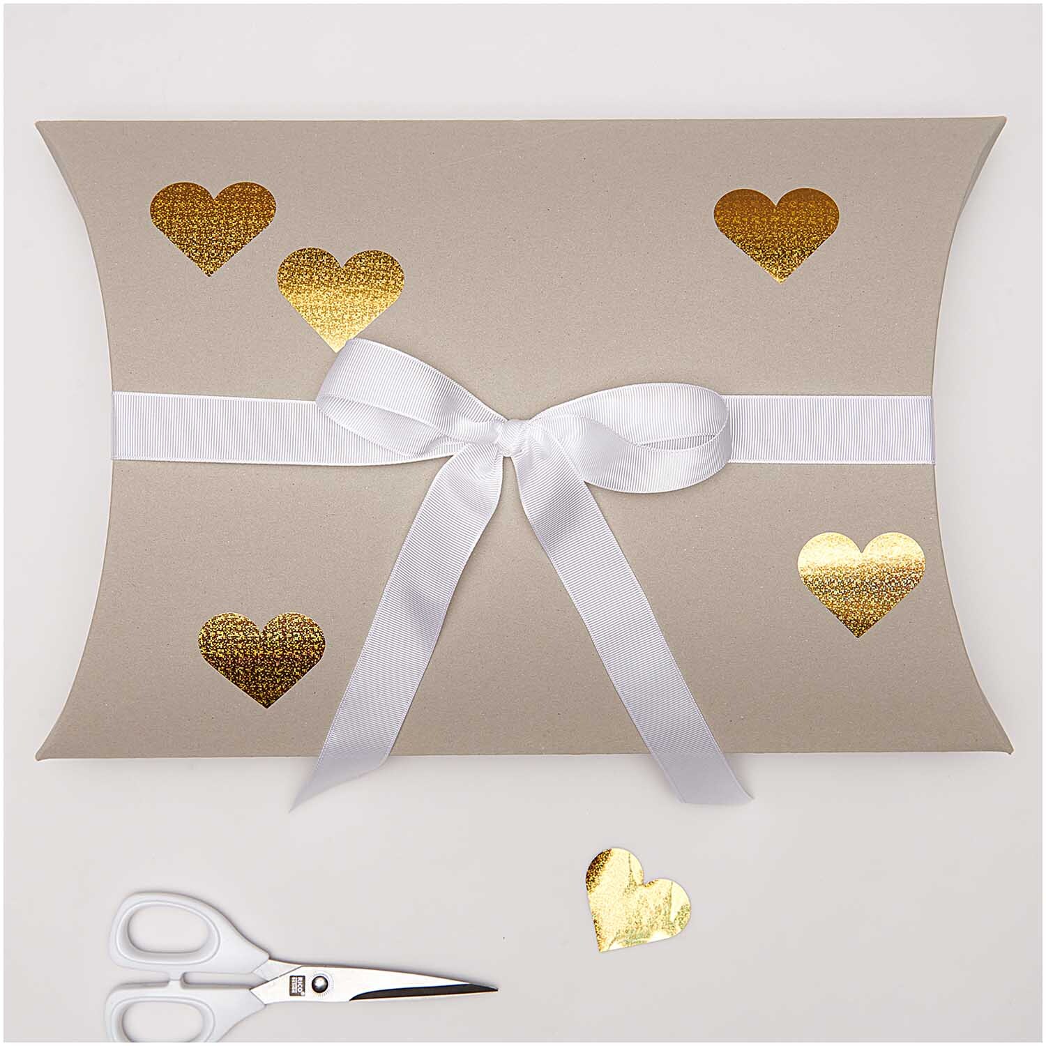 Paper Poetry Sticker Herzen auf Geschenkbox mit goldenen, holographischen Herzen und weißer Schleife. Schere im Vordergrund.
