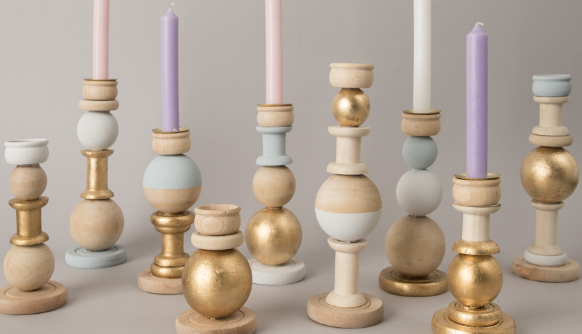 Bastelanleitung Kerzenhalter aus Holz: Verschiedene Kerzenhalter in Pastell- und Goldtönen auf grauem Hintergrund.