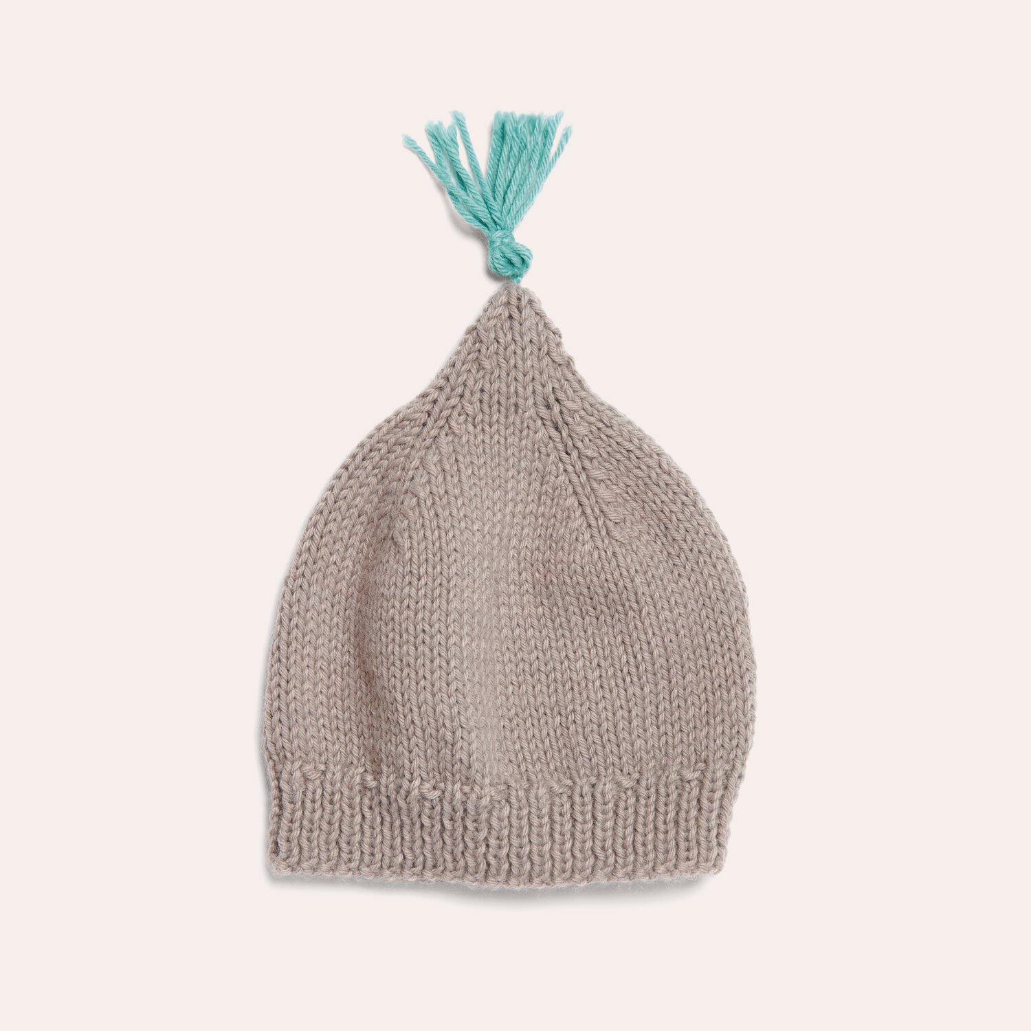 Strickset Mütze Modell 16: Beigefarbene gestrickte Babymütze mit türkisfarbenem Bommel auf hellem Hintergrund.