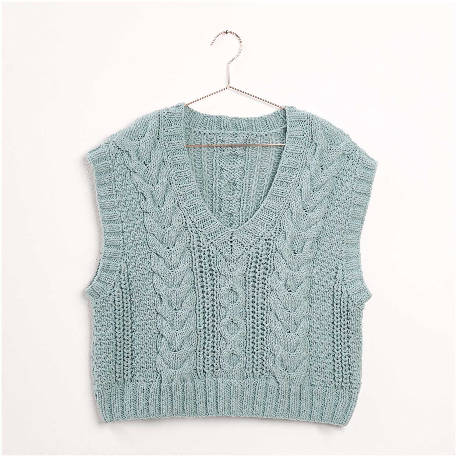 Ein hellblauer Strickpullunder von "Die Neue Masche", Modell 21 aus Heft Nr. 7, hängt an einem Kleiderbügel. Das Design zeigt ein Zopfmuster und ist ideal für stilvolle, handgemachte Mode.