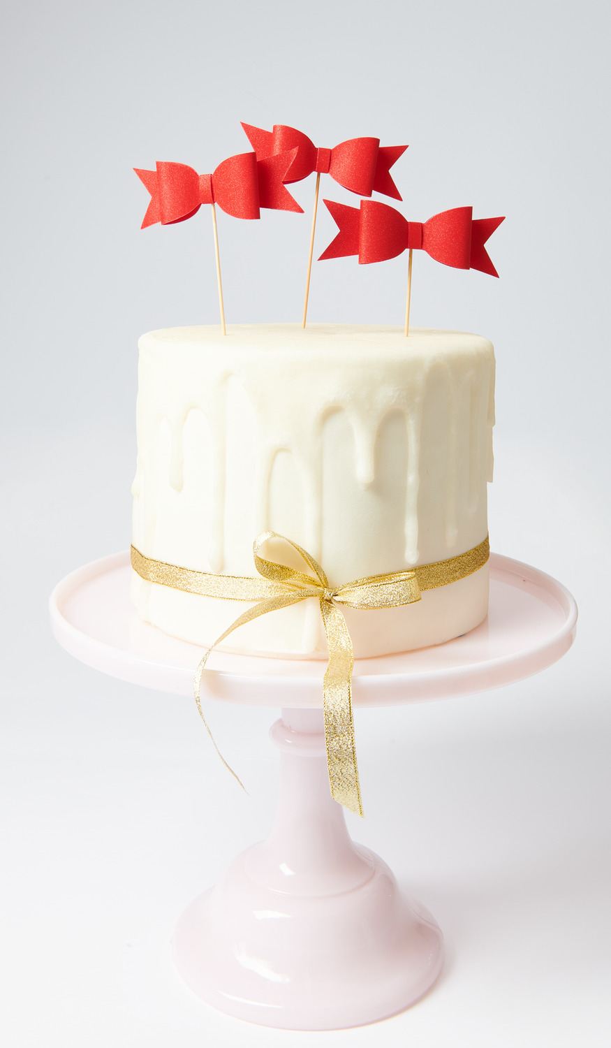Picker Schleife Rot auf einer weißen Torte mit goldener Schleife, präsentiert auf einem rosa Tortenständer.