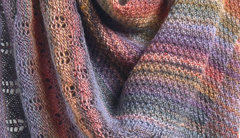 Strickanleitung Tuch aus Creative Melange aran Wonderball: Nahaufnahme eines bunten, gestrickten Tuchs mit detailreichem Muster in warmen Farbtönen.