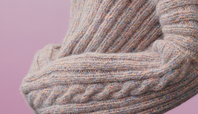 Strickanleitung Pullover aus Fashion Alpaca Bling Bling: Nahaufnahme eines gestrickten Pullovers mit Zopfmuster in sanften Pastelltönen vor rosa Hintergrund.