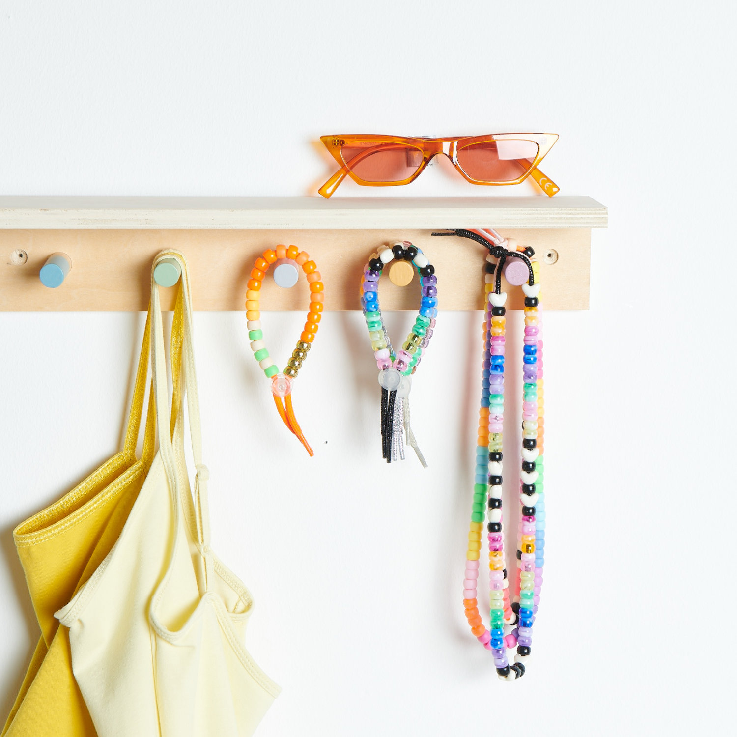 An einer Wandgarderobe zwei hängende Armbänder und zwei hängende Ketten aus verschiedenen bunten Perlen und Bändern.