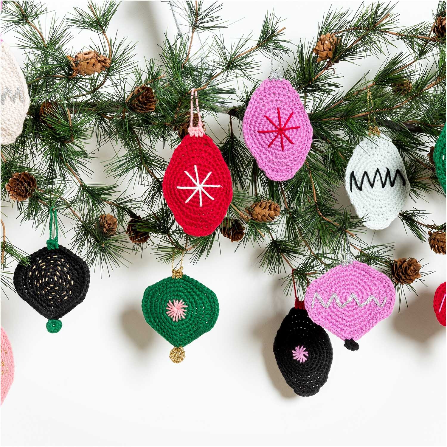 Creative Ricorumi Lamé dk: Bunte, gehäkelte Weihnachtsornamente an einem Tannenzweig, ideal für festliche Dekorationen.