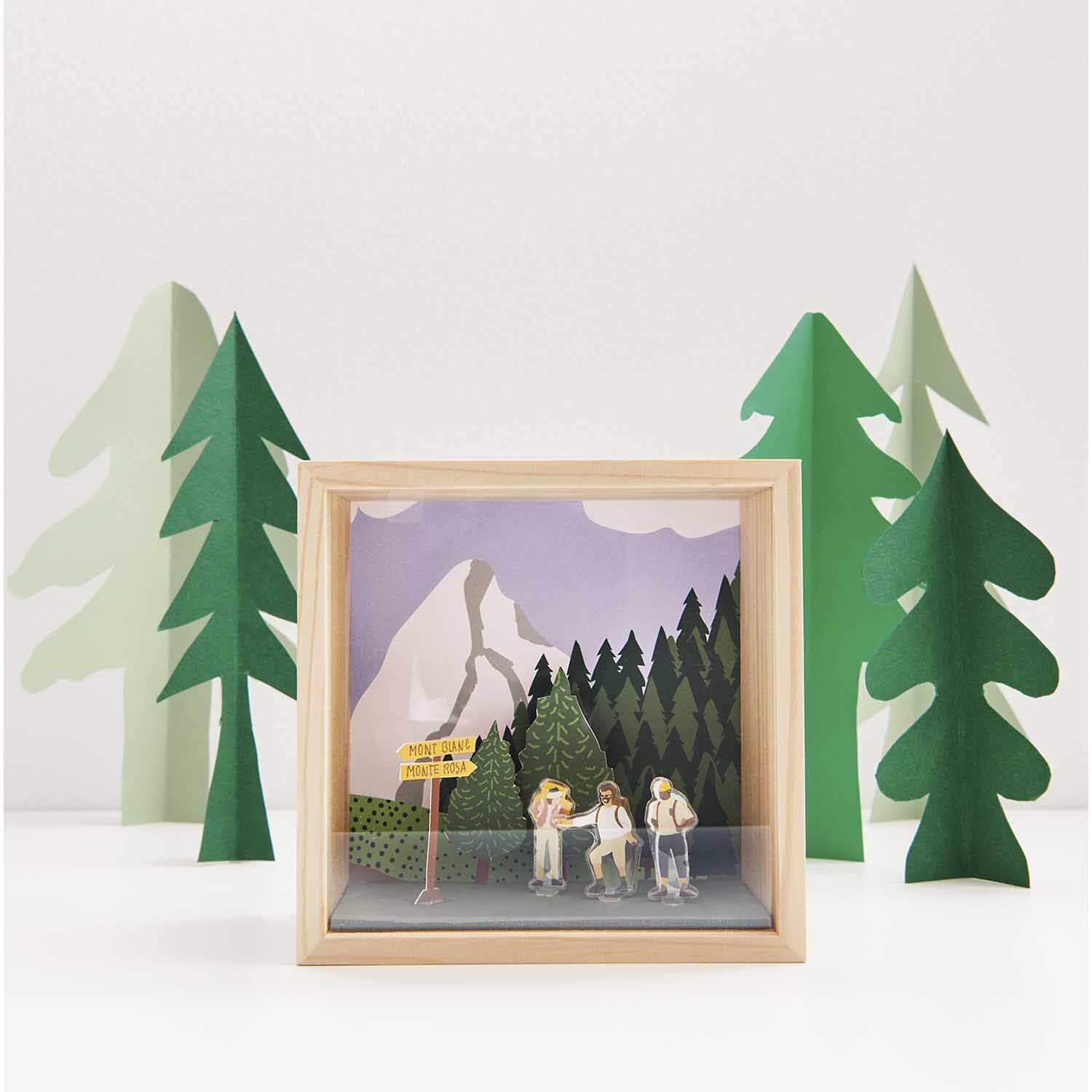 Figurico Gelsticker Outdoor Aktivitäten: Holzrahmen mit Berglandschaft und Wanderern, umgeben von grünen Bäumen. Ideal für kreative Dekorationen.