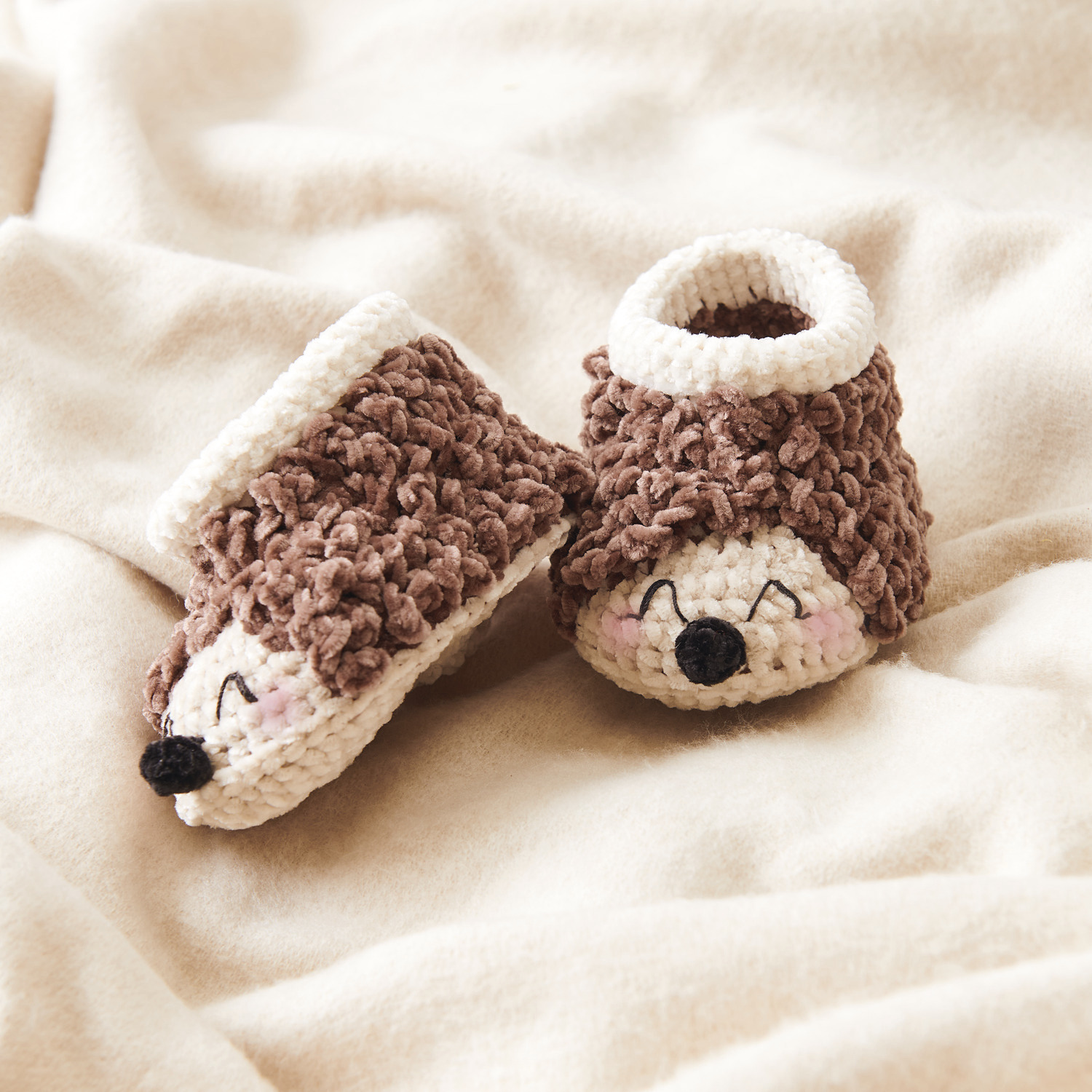 Ricorumi Häkelset Baby Booties Igel, creme und schokoladenfarbene Häkel-Babyschuhe in Igel-Design auf weicher Decke.