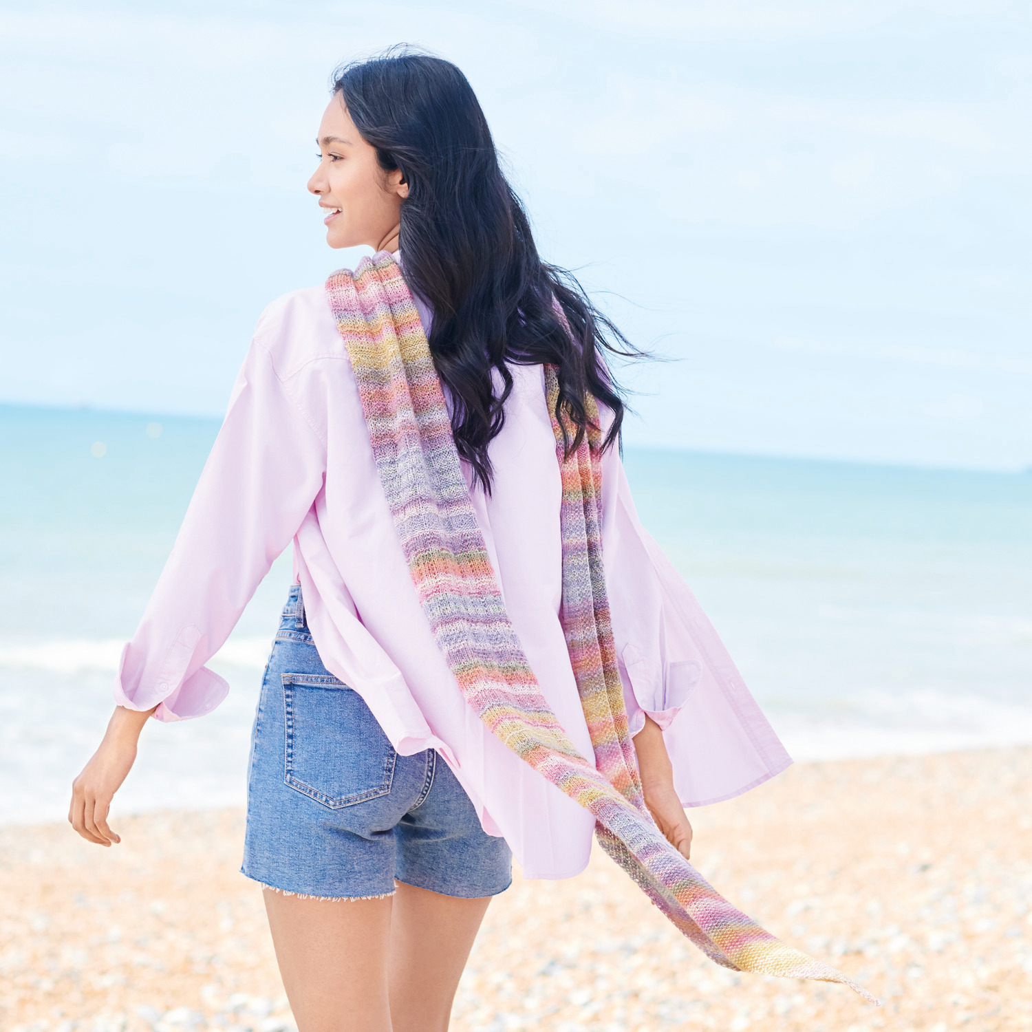 Fashion Cotton Merino Lace Strickset: Frau am Strand mit buntem Tuch, lässig über die Schulter gelegt.