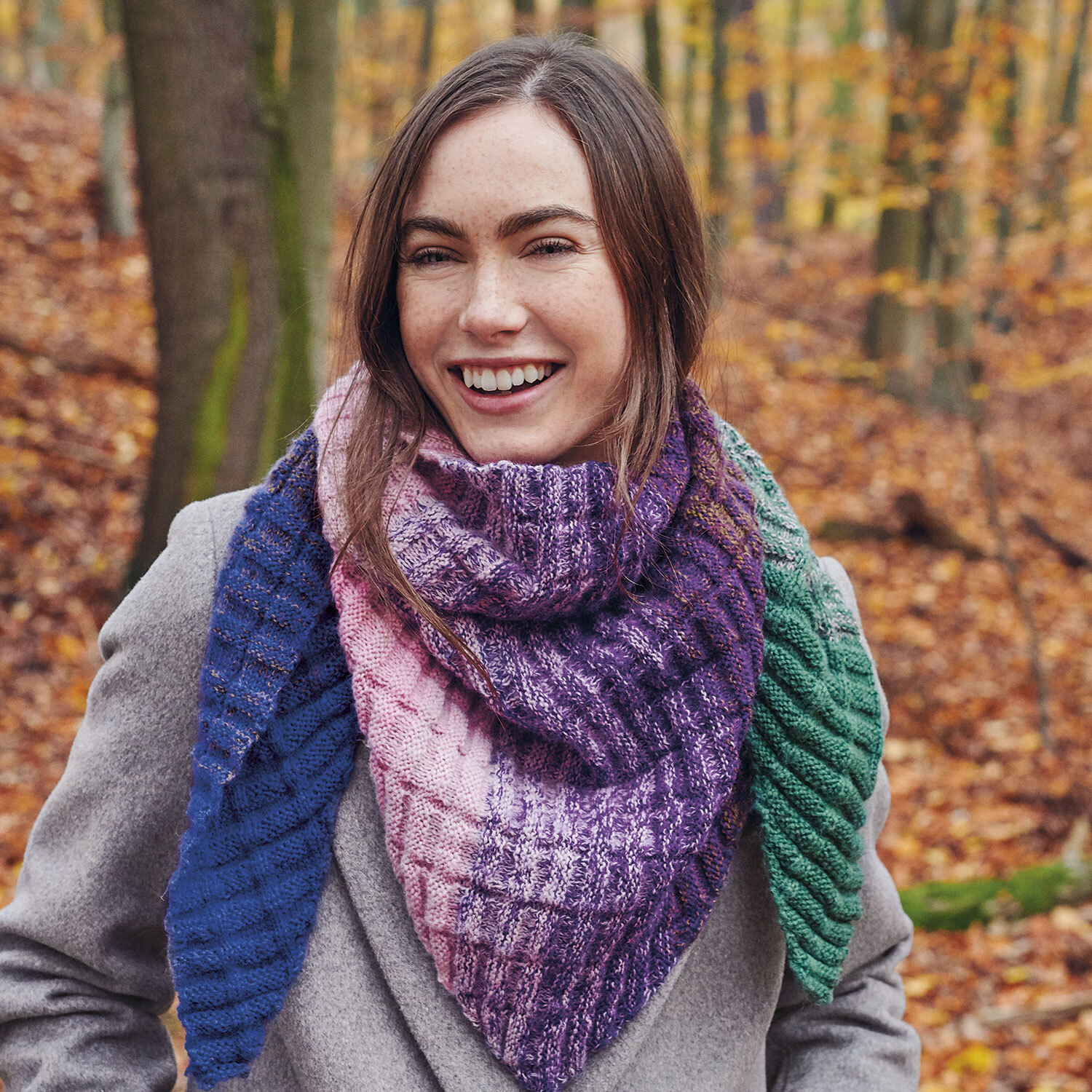 Eine Frau trägt einen gestrickten Schal in Dreiecksform aus einem Farbverlaufsgarn.