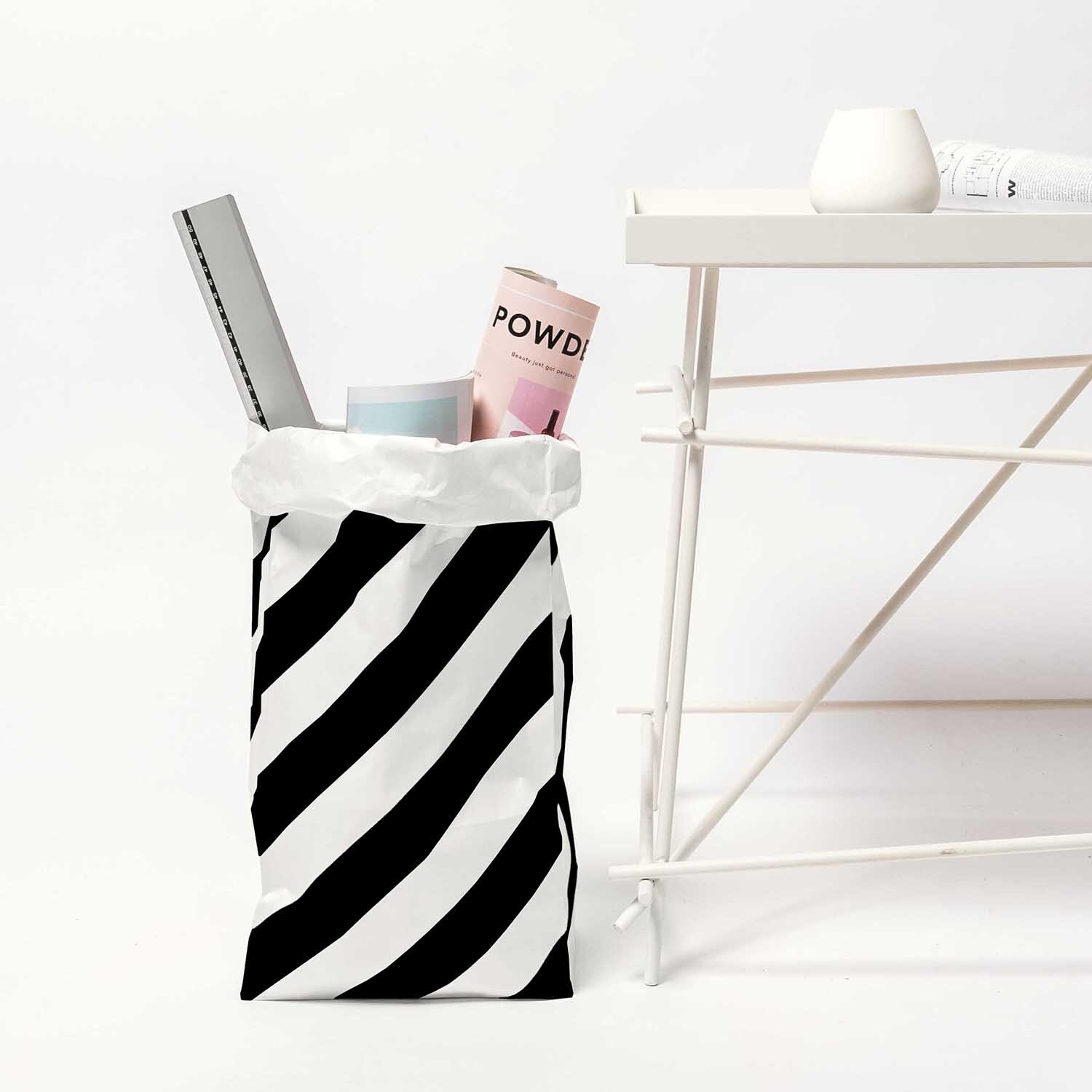 Paper Poetry Maxi-Blockbodenbeutel M mit Streifen, gefüllt mit Magazinen, neben weißem Tisch.