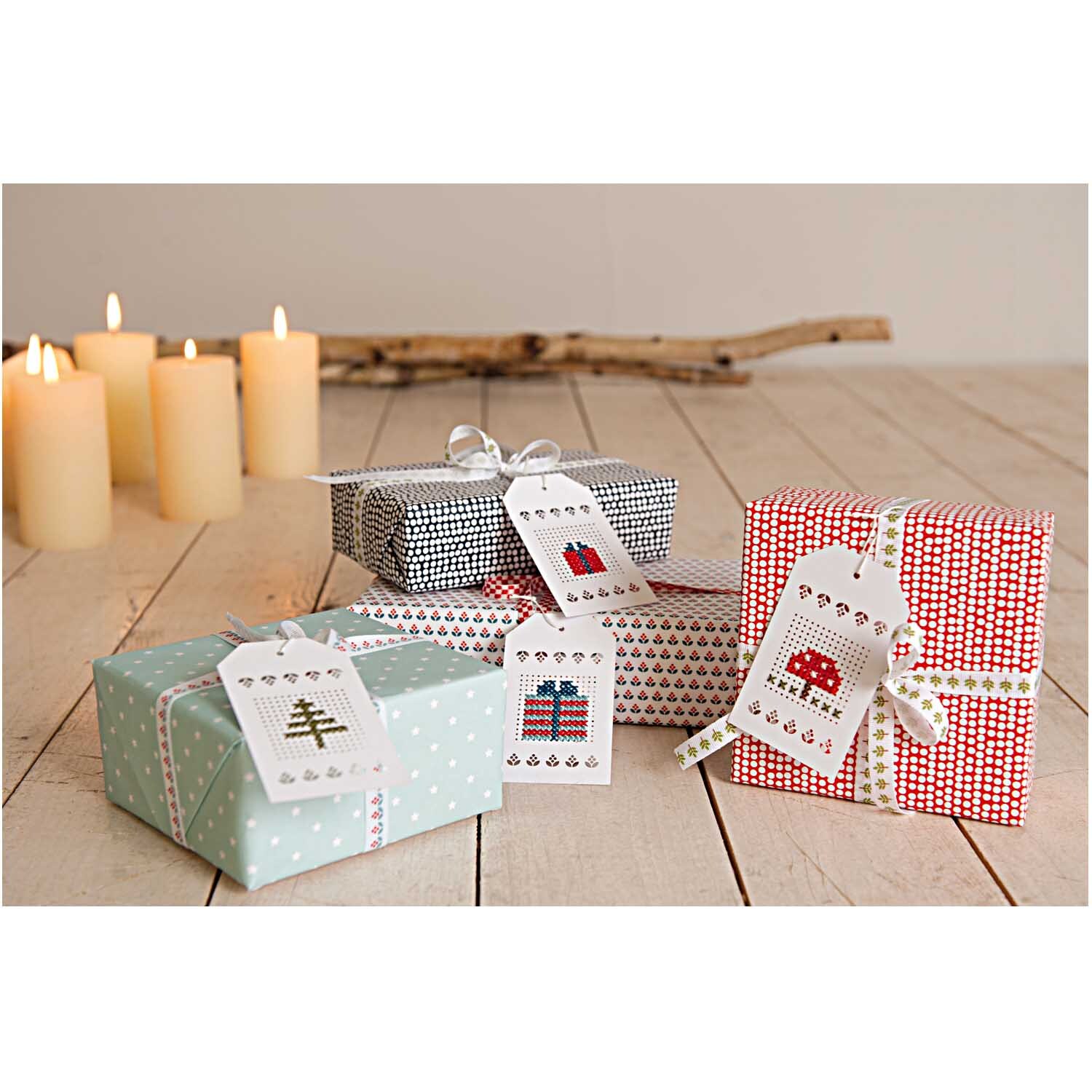 Anhänger zum Besticken in creme von Rico Design, dekoriert auf Geschenken neben brennenden Kerzen.