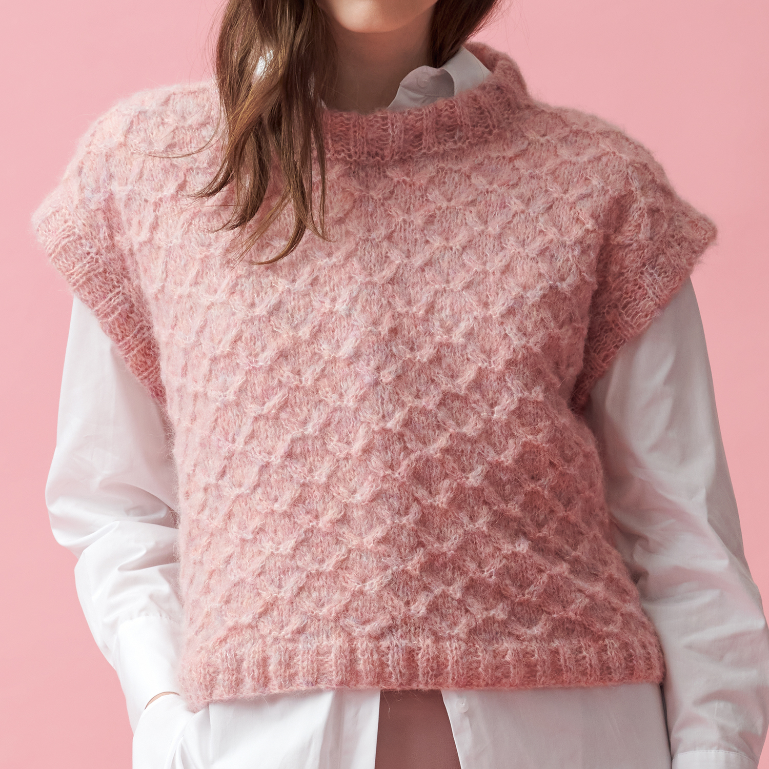 Strickanleitung Pullunder aus Fashion Skinny Alpaca aran: Rosa Pullunder über weißer Bluse vor rosa Hintergrund.