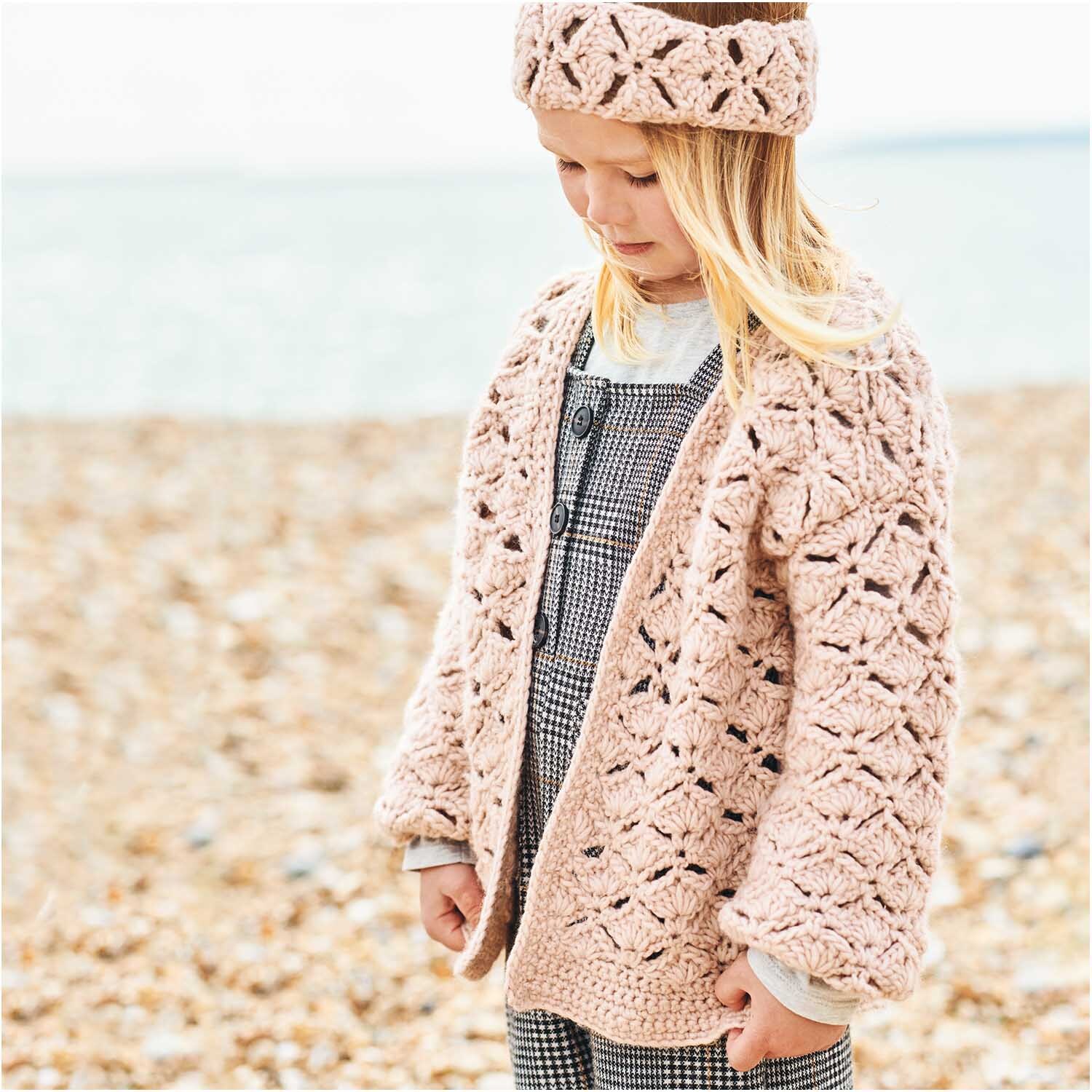 Essentials Super aran: Kind am Strand in gestricktem Cardigan und Stirnband aus Rico Design Wolle.