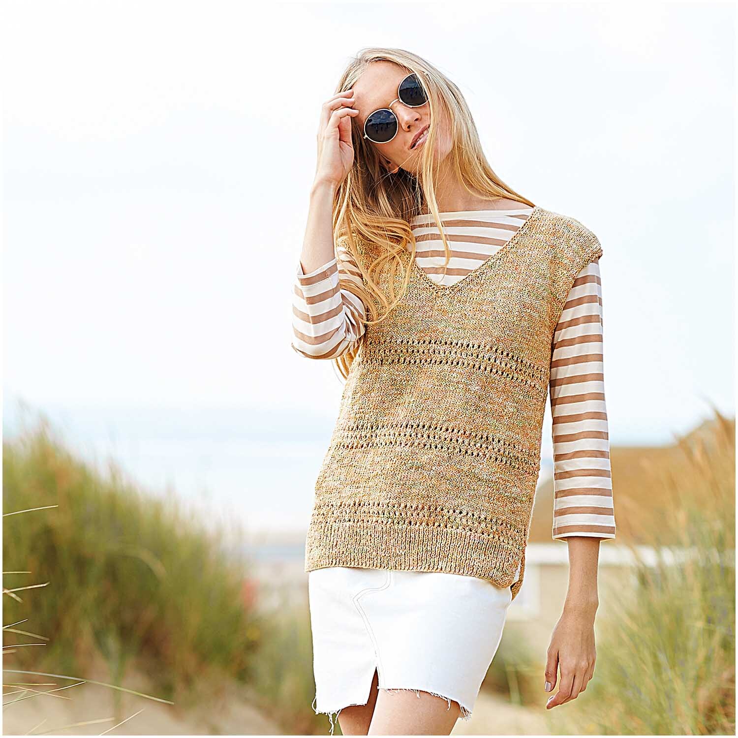 Creative Cotton Zickzack: Frau am Strand in gestricktem Oberteil, kombiniert mit gestreiftem Shirt und Sonnenbrille. Ideal für sommerliche Tage.