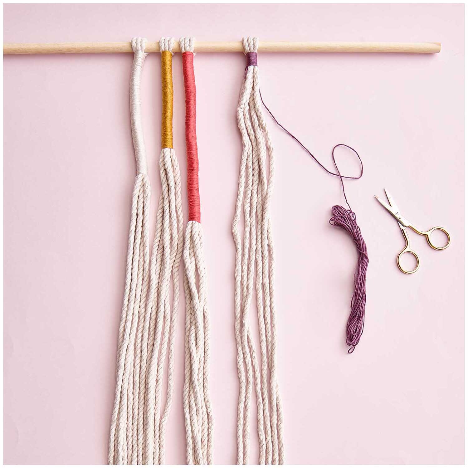 Stickgarn Set Earthy: Mehrfarbiges Garn von Rico Design, 10-teilig, mit Schere auf rosa Hintergrund.