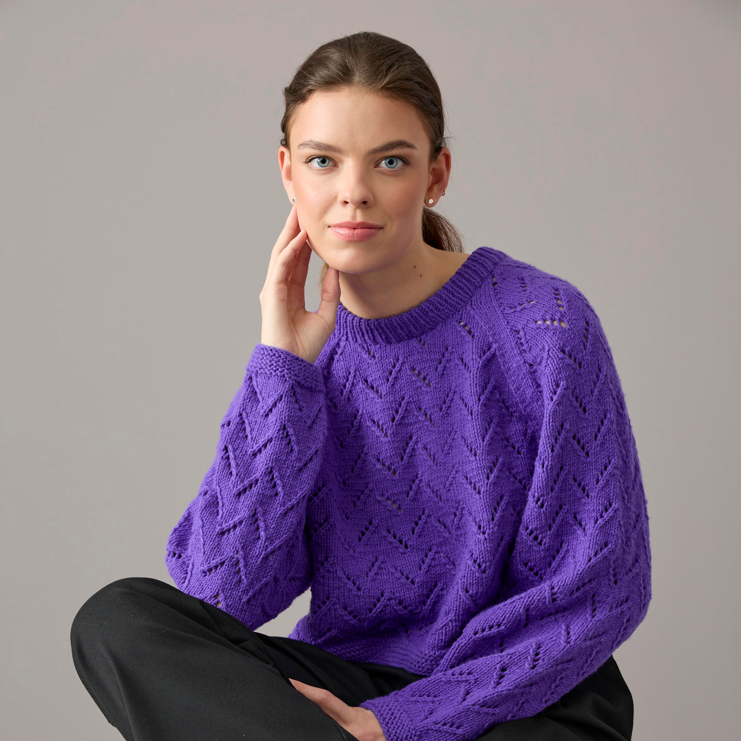 Pullover aus Vegan Cashmere in Violett von Rico Design, getragen von einer Frau vor grauem Hintergrund.