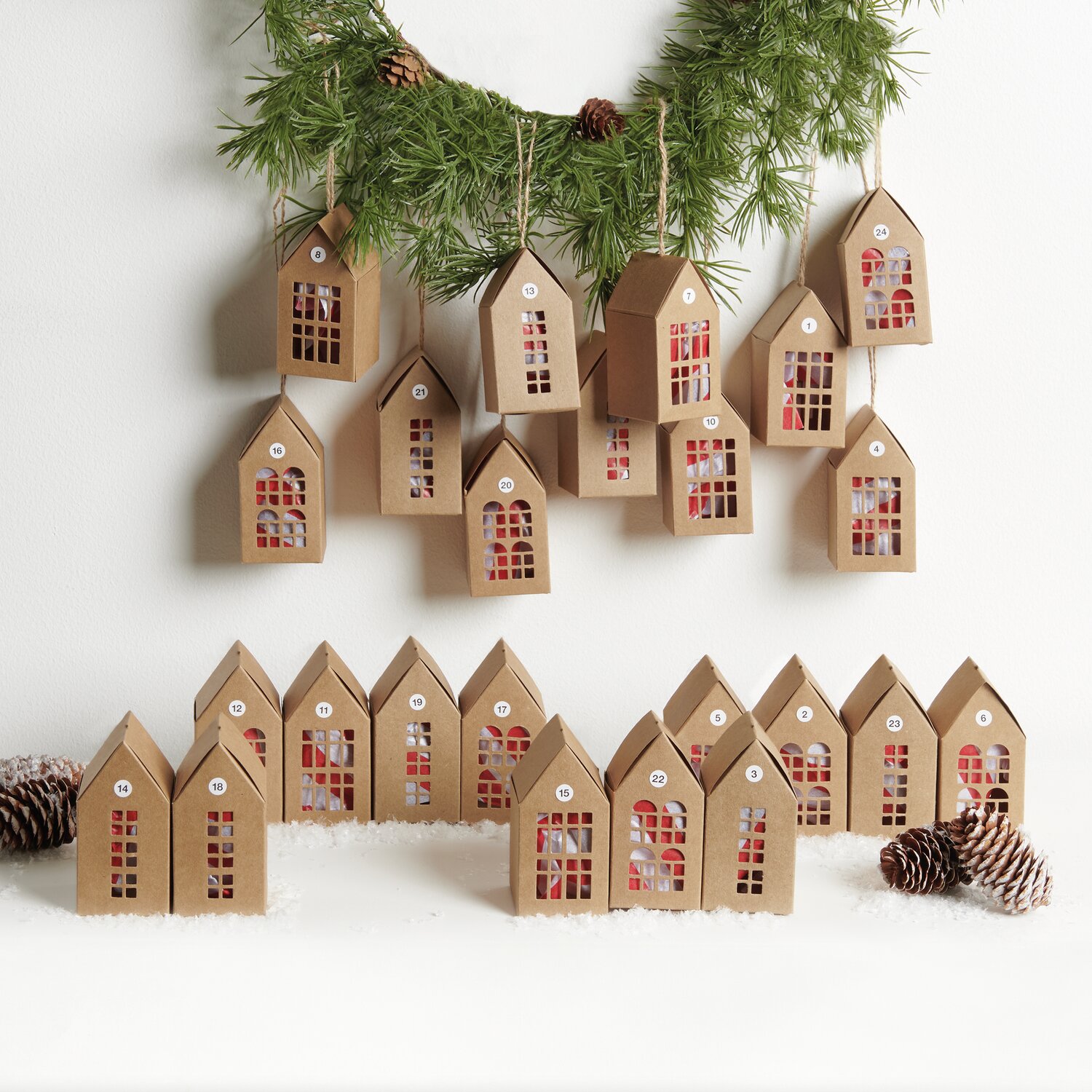 Adventskalender Papphäuser 24 Stück aus Kraftpapier, dekorativ arrangiert mit Tannenzweigen.