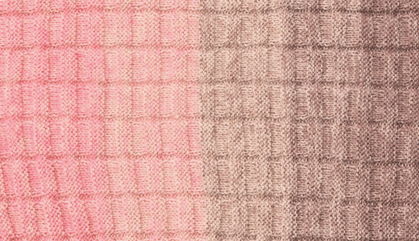 Strickanleitung Dreieckstuch Creative Wool Dégradé Super 6: Nahaufnahme eines gestrickten Stoffes in Rosa- und Beigetönen mit einem karierten Muster.
