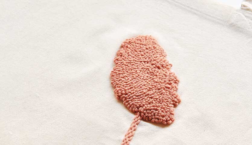 Anleitung Jutebeutel mit der Punch Needle gestalten: Nahaufnahme eines beigen Stoffes mit rosa Stickerei in Blattform.