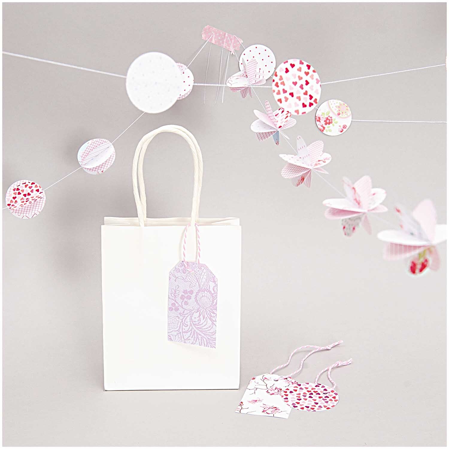 Paper Poetry Motivpapier Block Floral zeigt eine weiße Geschenktüte mit bunten Papierdekorationen.