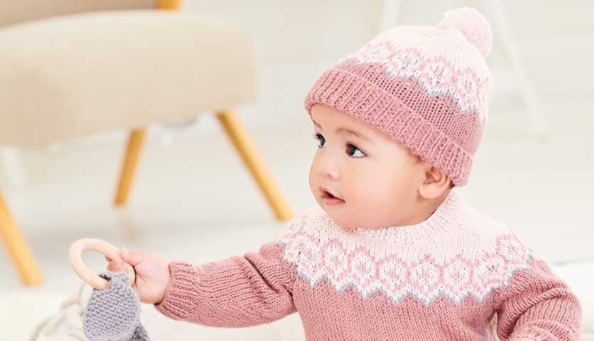 Strickanleitung Mütze und Pullover aus Rico Baby Dream dk Uni: Baby in rosa-weißem Strickset.
