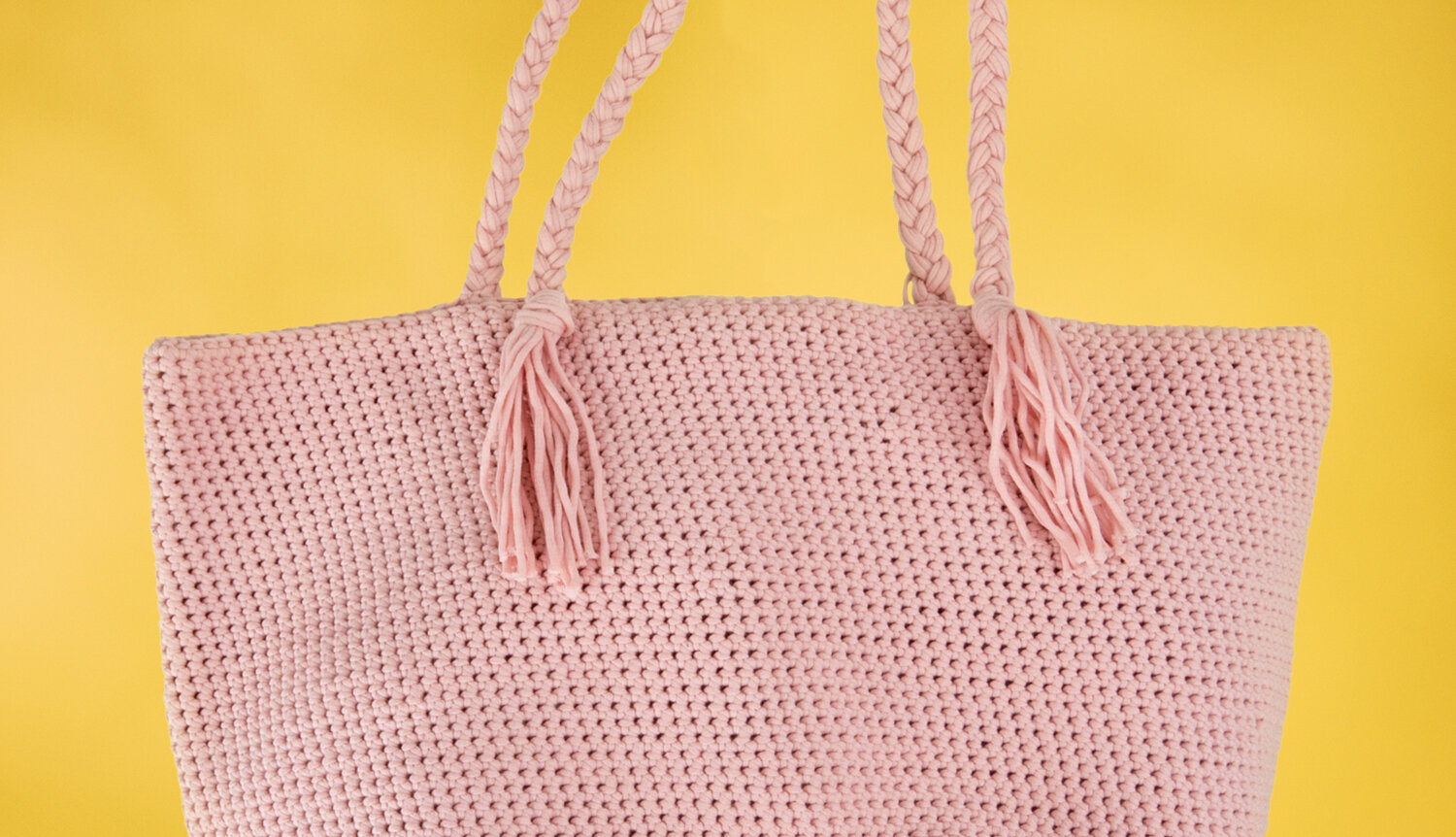 Häkelanleitung Tasche aus Fashion Jersey, große gehäkelte Tragetasche mit langen Henkeln und Quasten vor kontrastierendem Hintergrund
